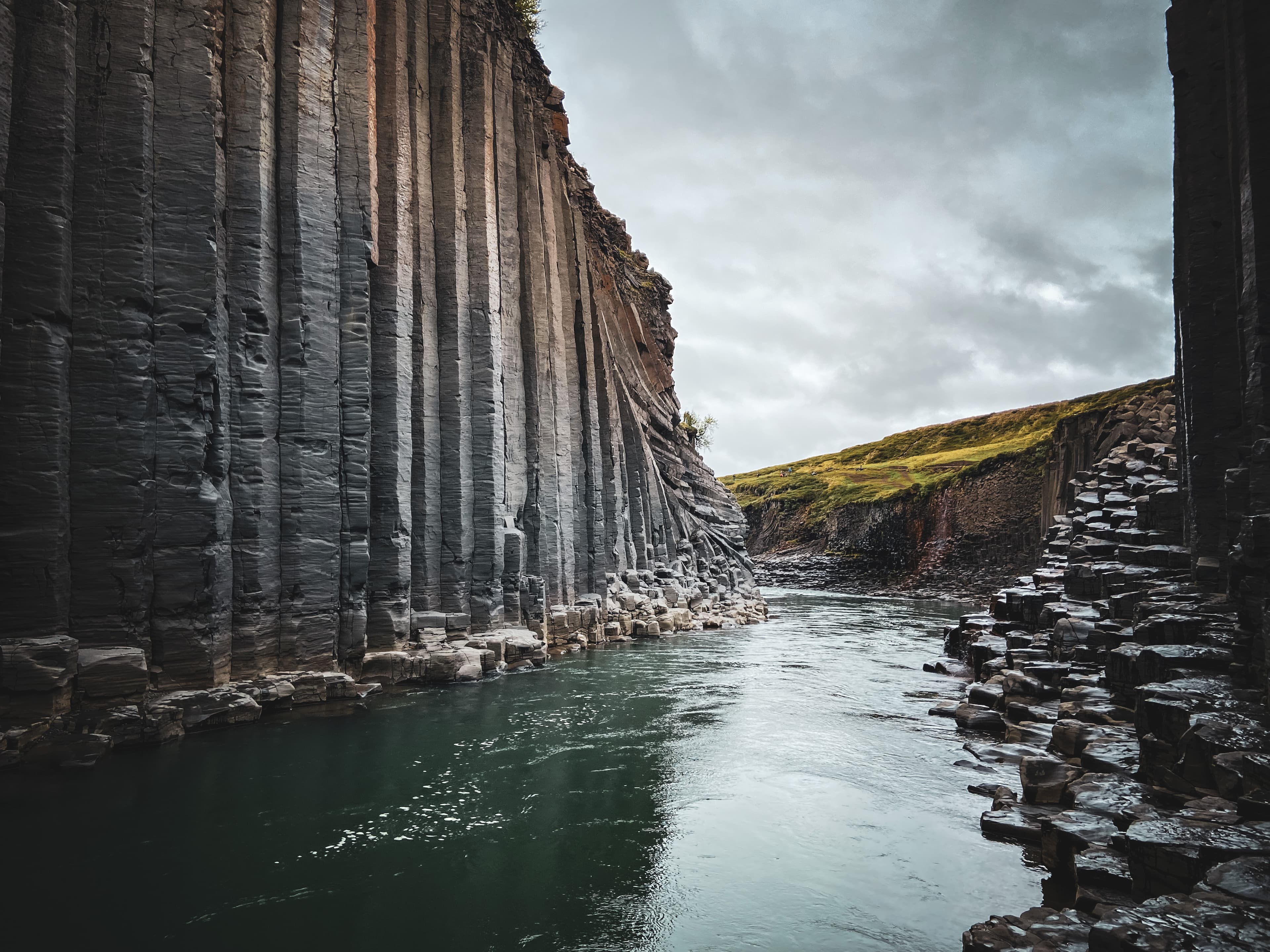 A grey stone cliff in Iceland with a green emerald river flowing through.