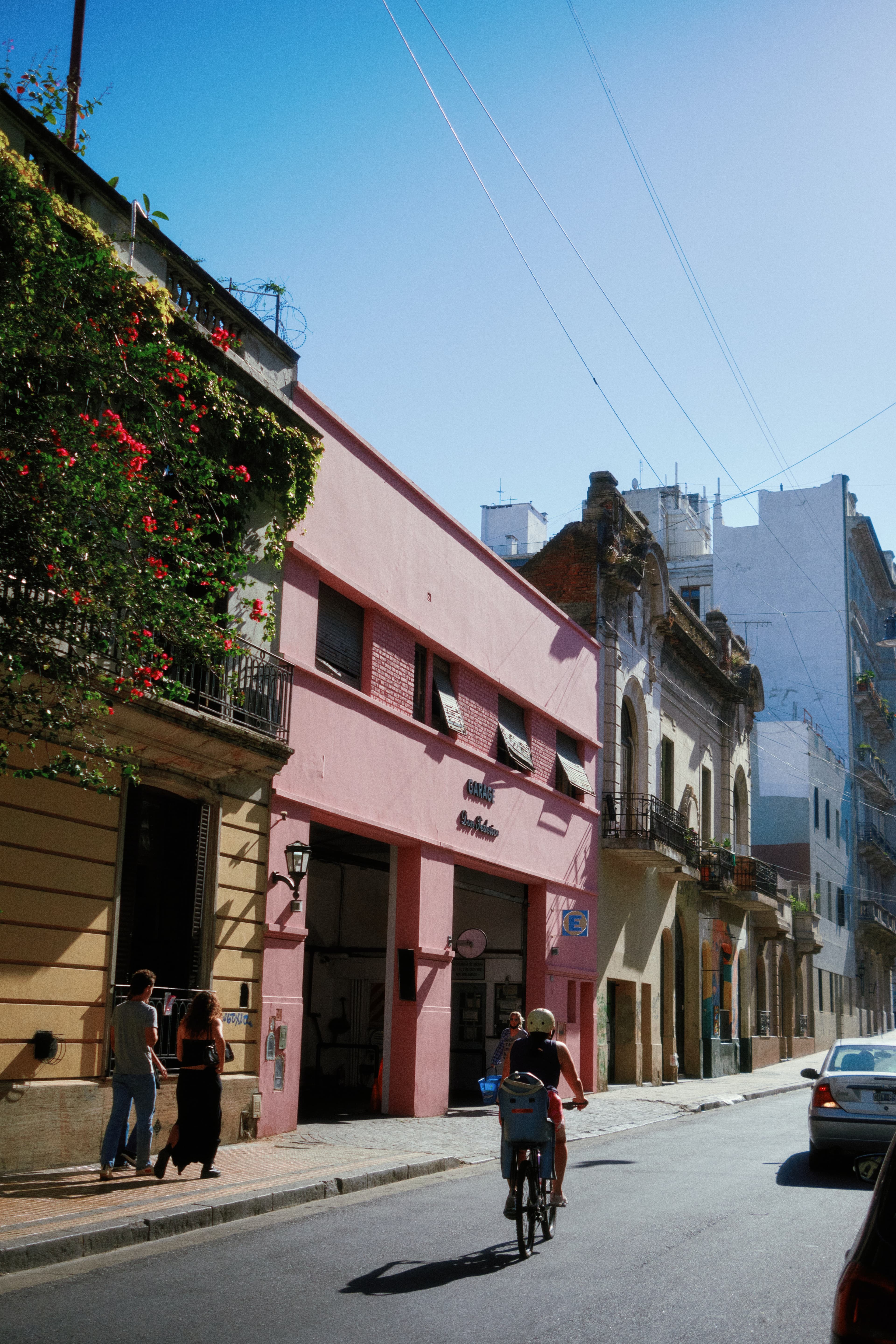 People on the street next to pink building on a sunny day