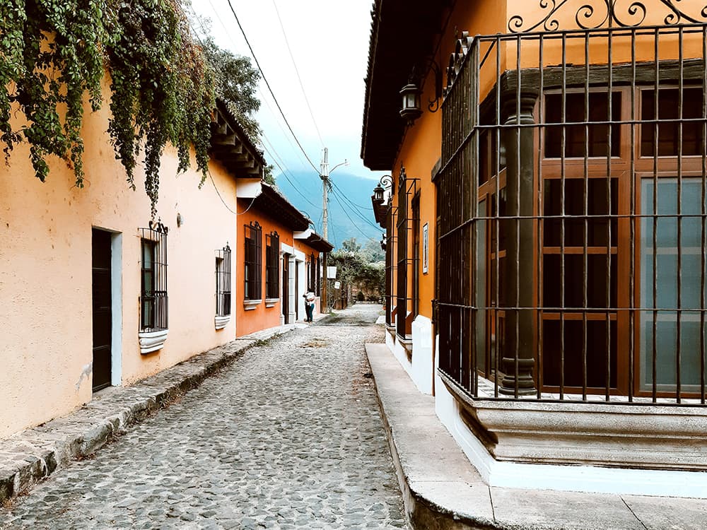 cobblestone streets in Guatemala with green vines and tan orange buildings with a black iron gate