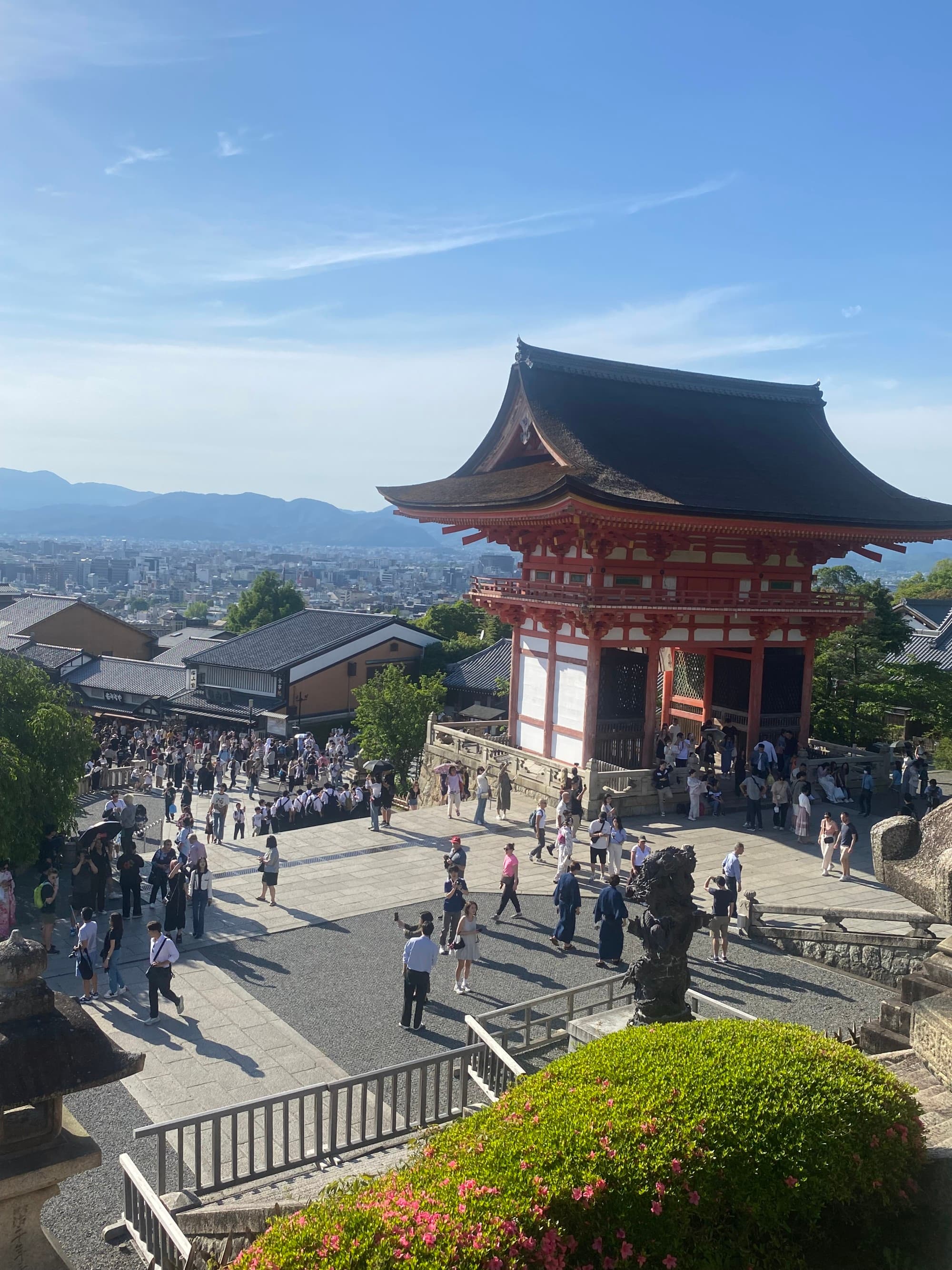 A view of a platform with tourists and a tall structure with Japanese architecture at Kiyomizu-Dera