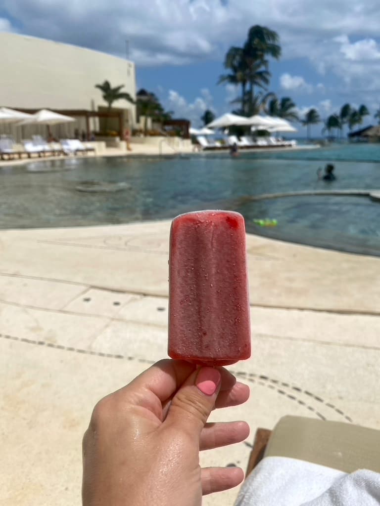 A person holding up a popsicle next to an outdoor pool