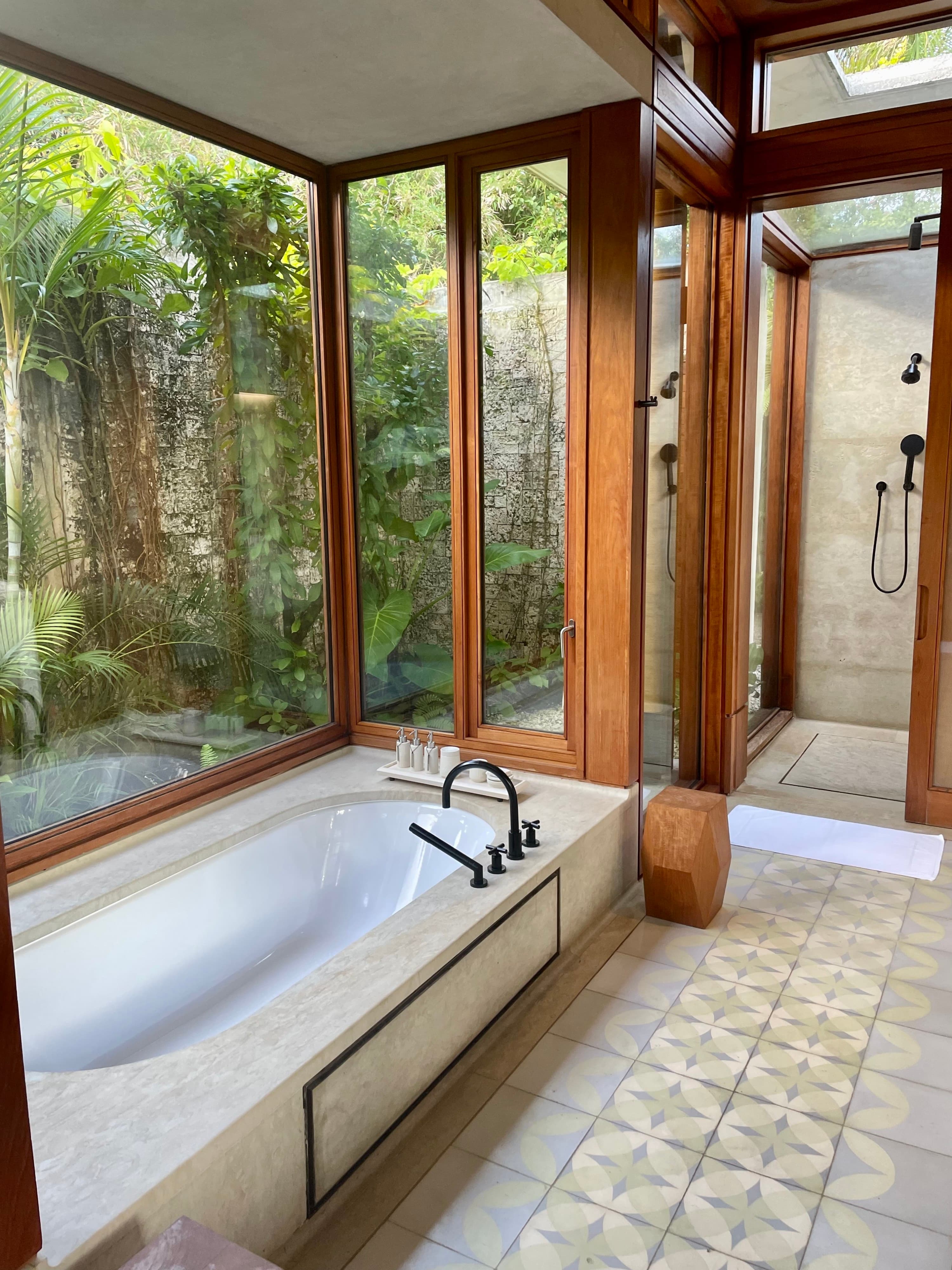 A sunken bathtub surrounded by windows with tropical jungle foliage outside.