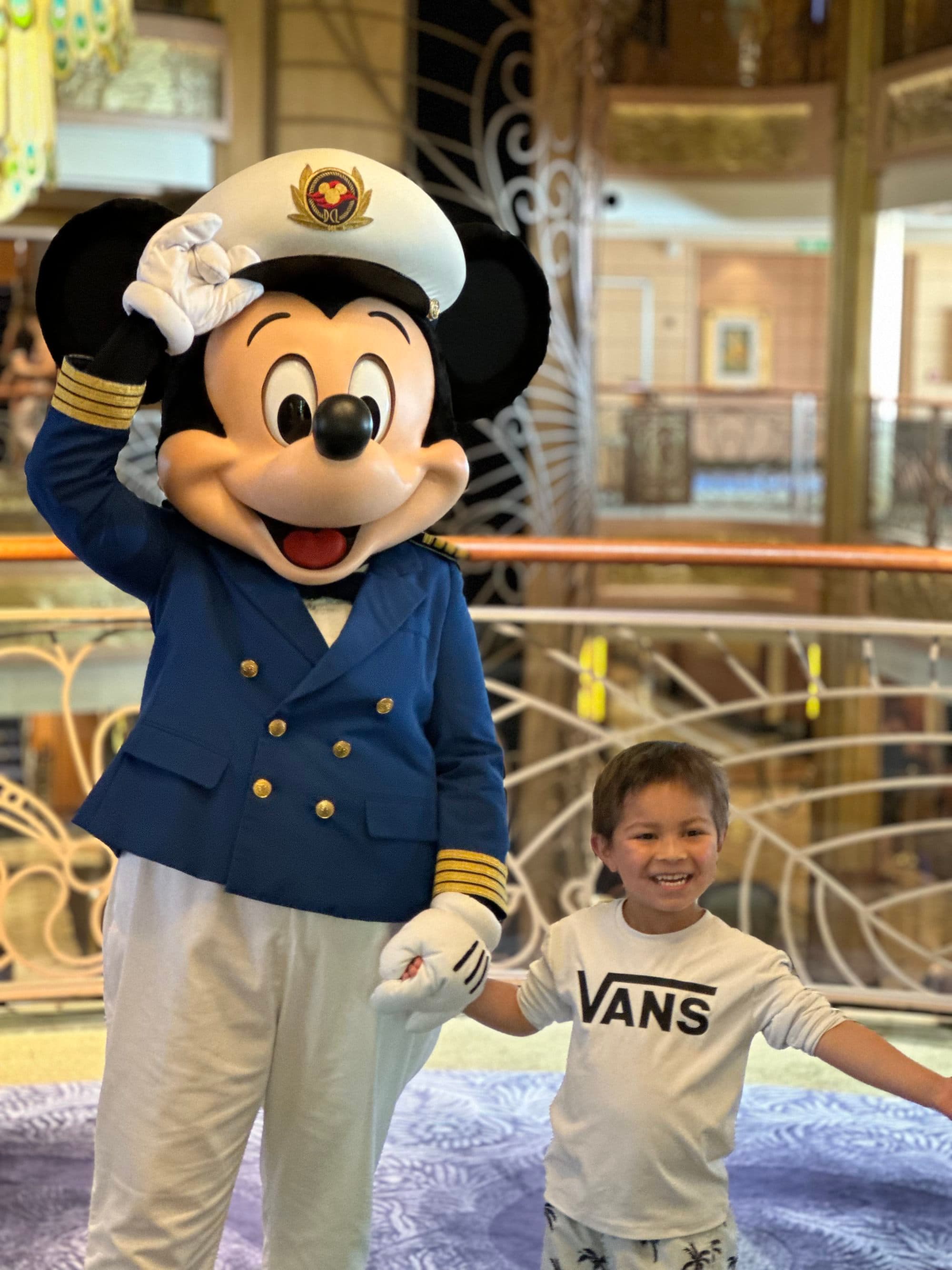 Mickey Mouse waves and holds hands with a young child wearing a Vans t-shirt.