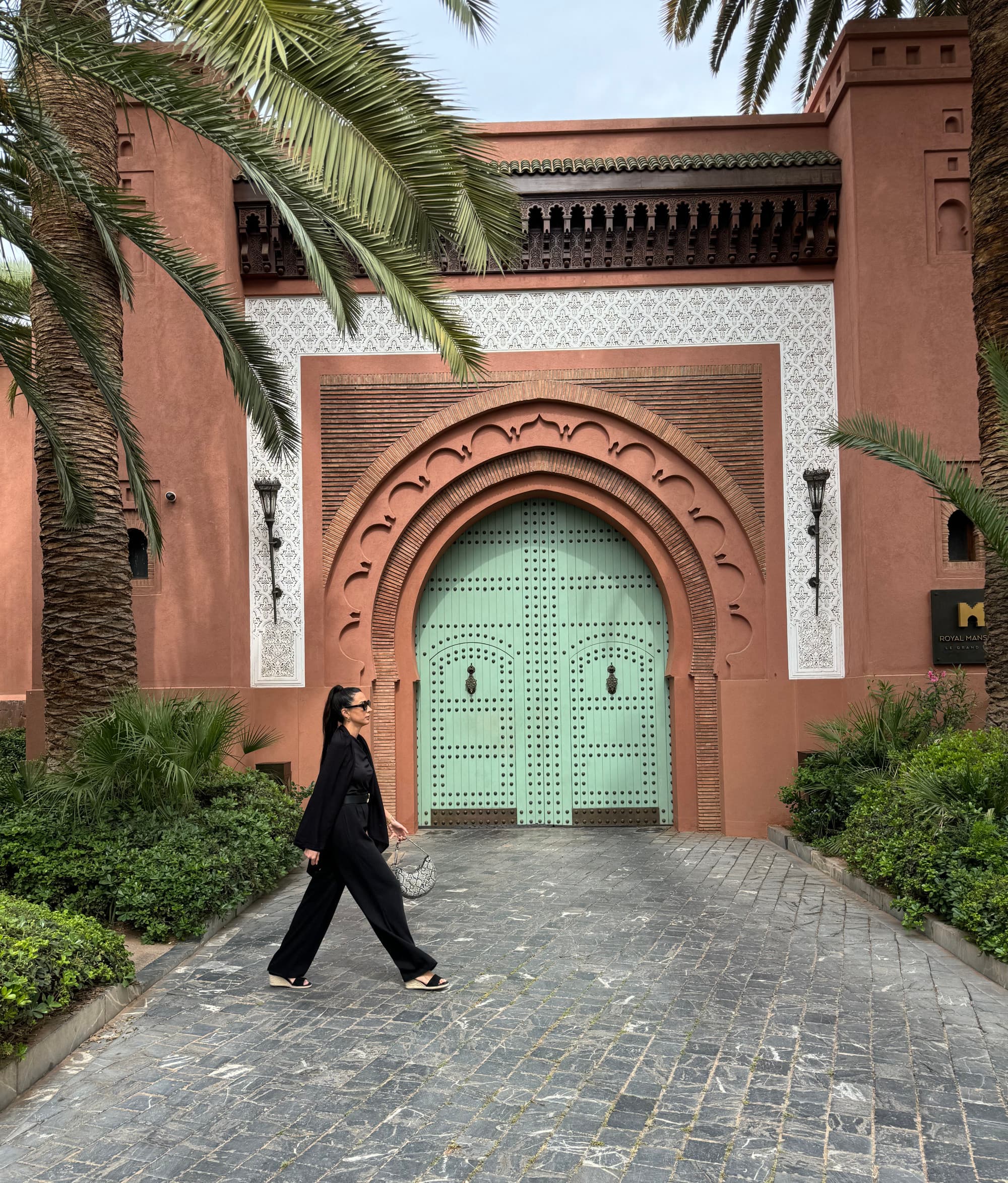 A person walking by a coral-colored wall with green doors