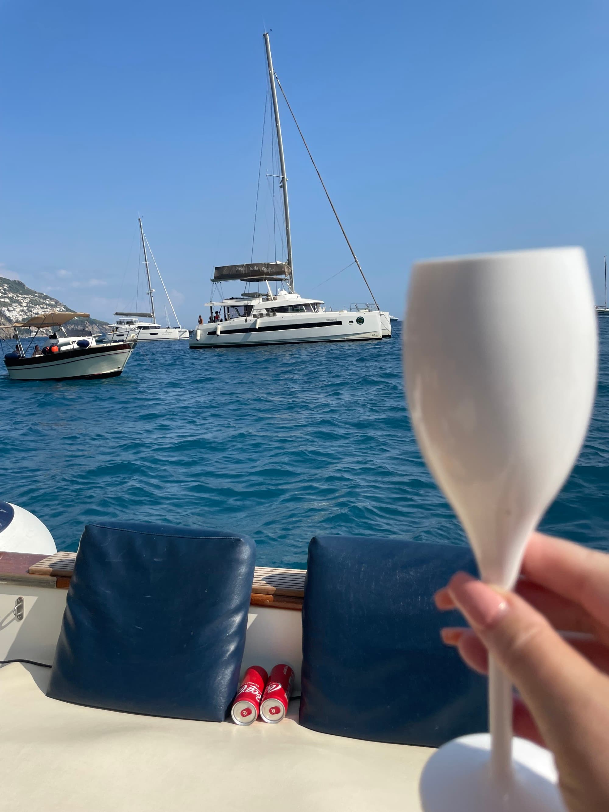 A hand holding up a white wine glass on a boat in the water