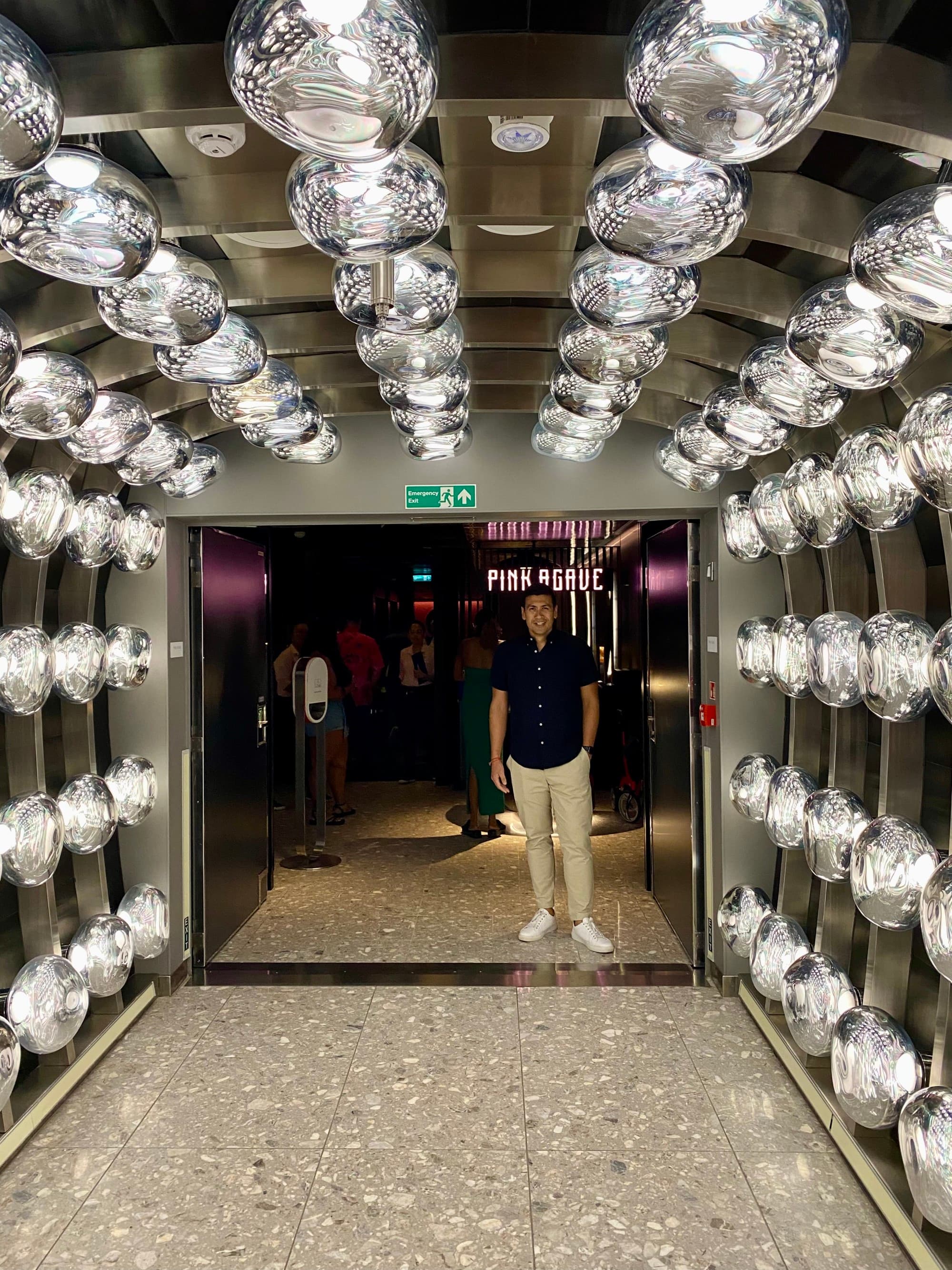 A person standing at the end of a hallway covered in light bulbs