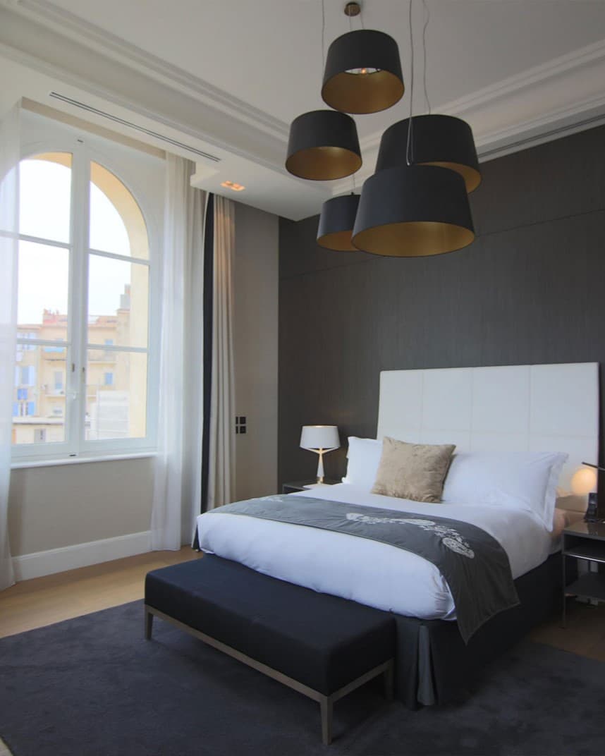A hotel room with a white bed and large windows