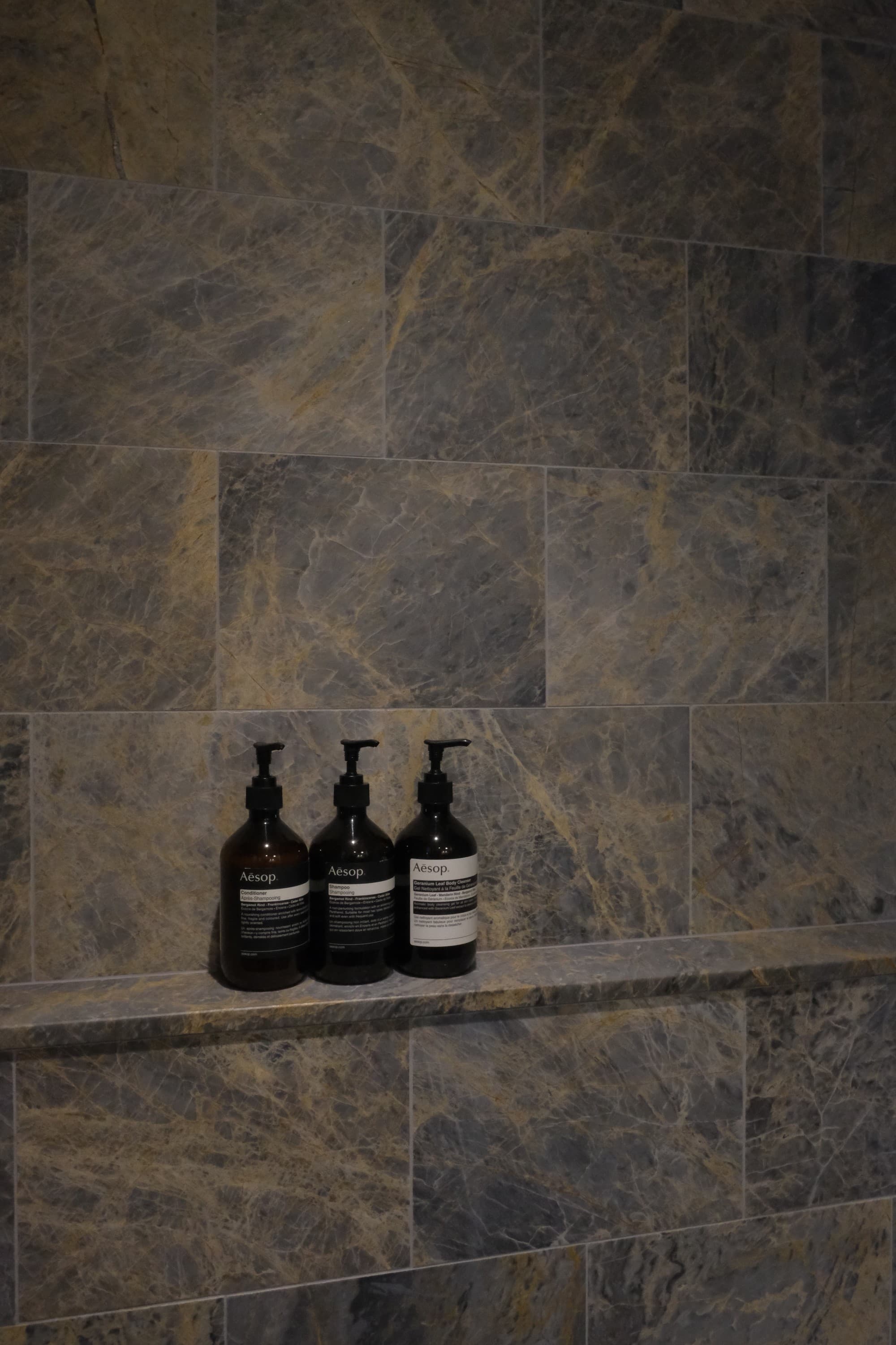 A spacious walk in shower with Blue Emperador marble and Aesop bath products.