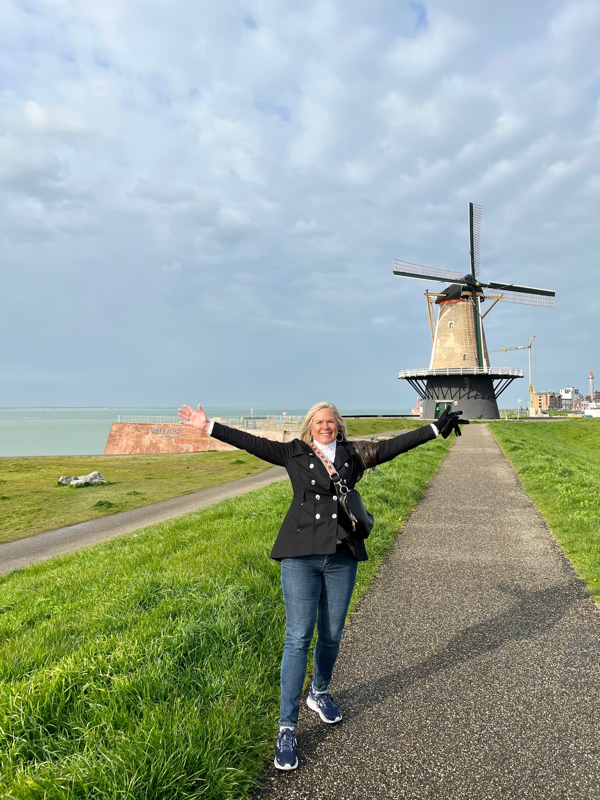 Advisor posing for a photo with outstretched arms in front of a windmill during the daytime