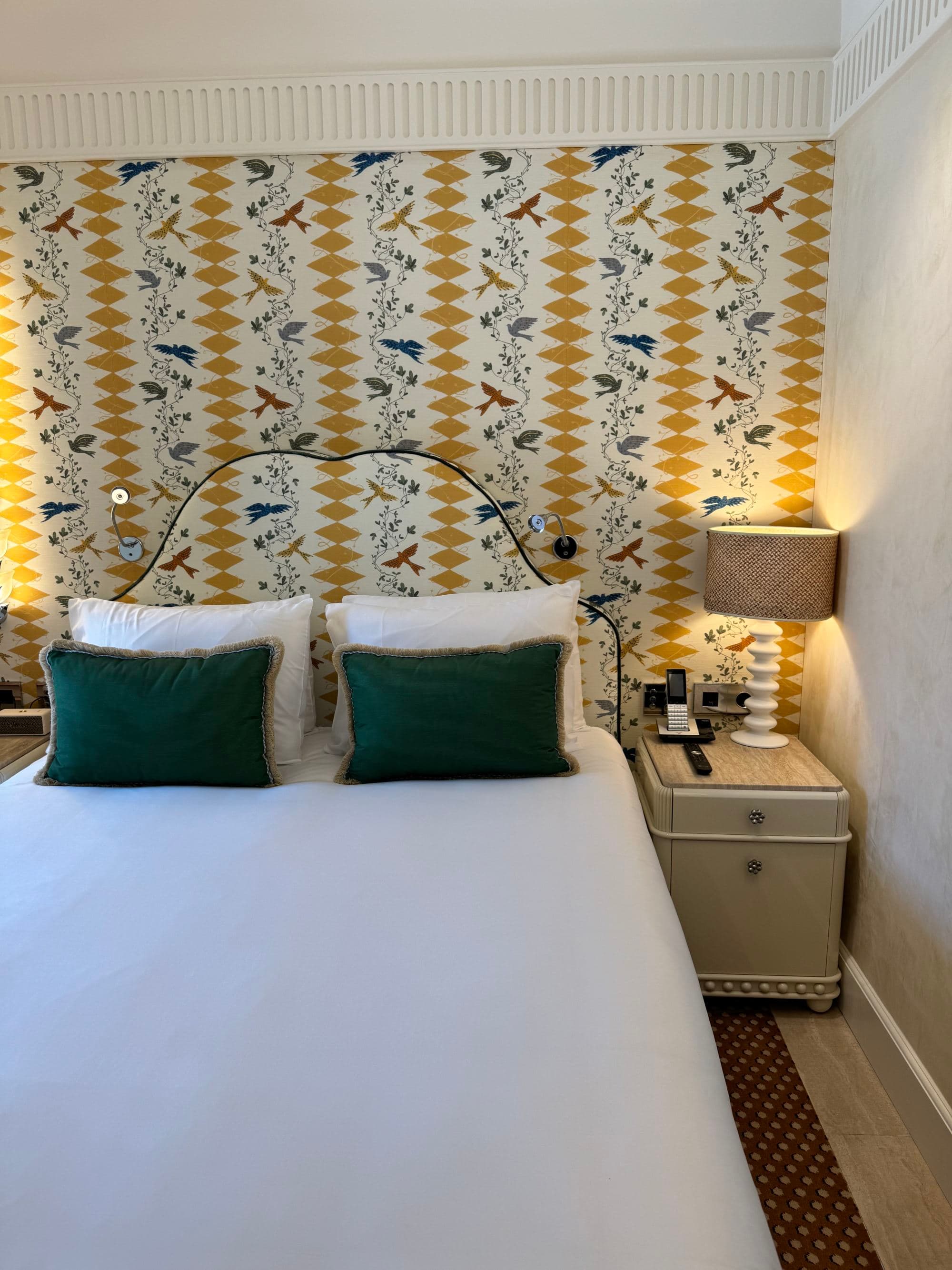 The view of another hotel bedroom with bright wallpaper and quaint furnishings.