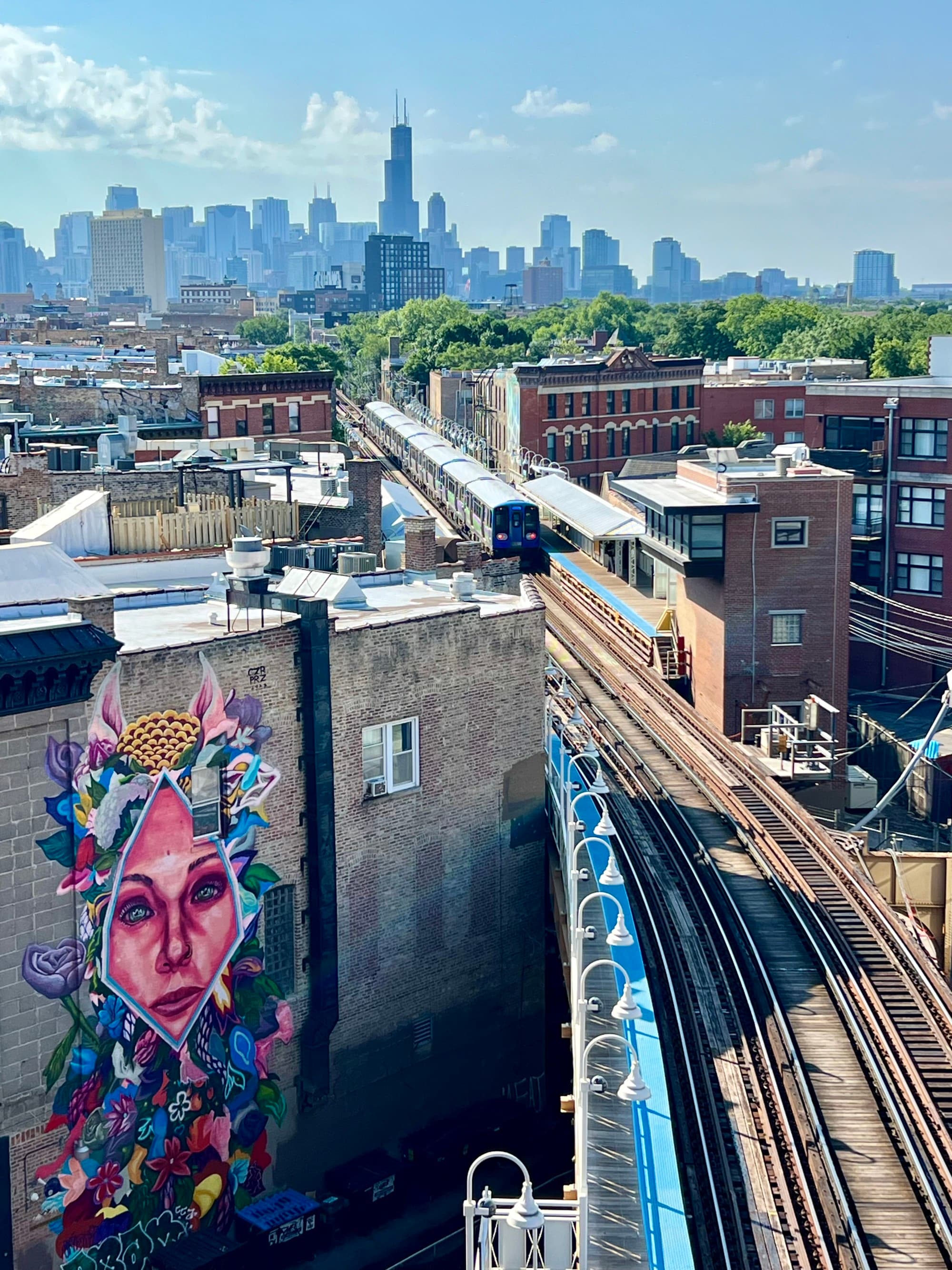 Skyline view overlooking train tracks with a mural of a woman's face on a nearby wall.