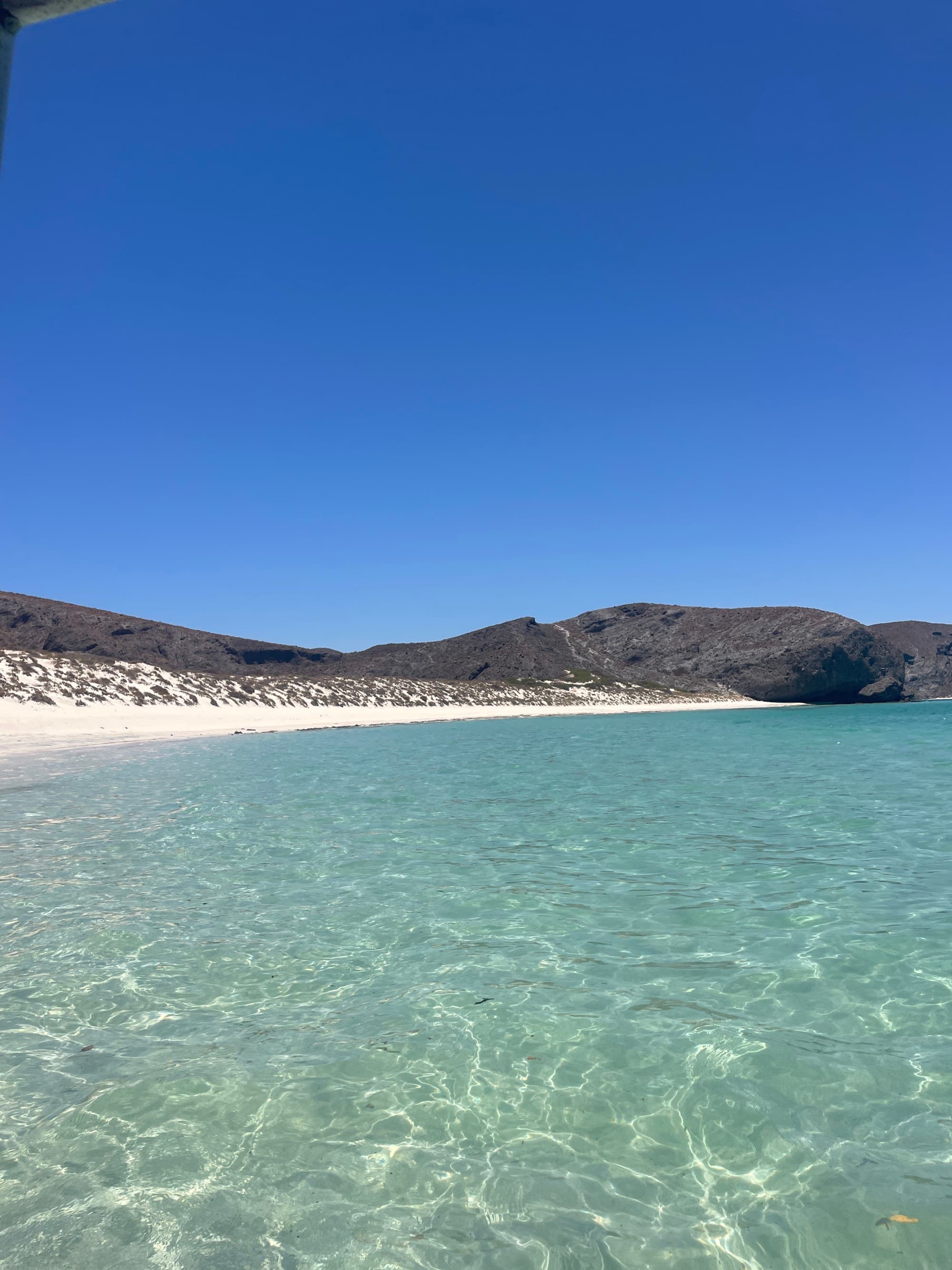Sea and seaside view with shallow blue water and white sandy beach.