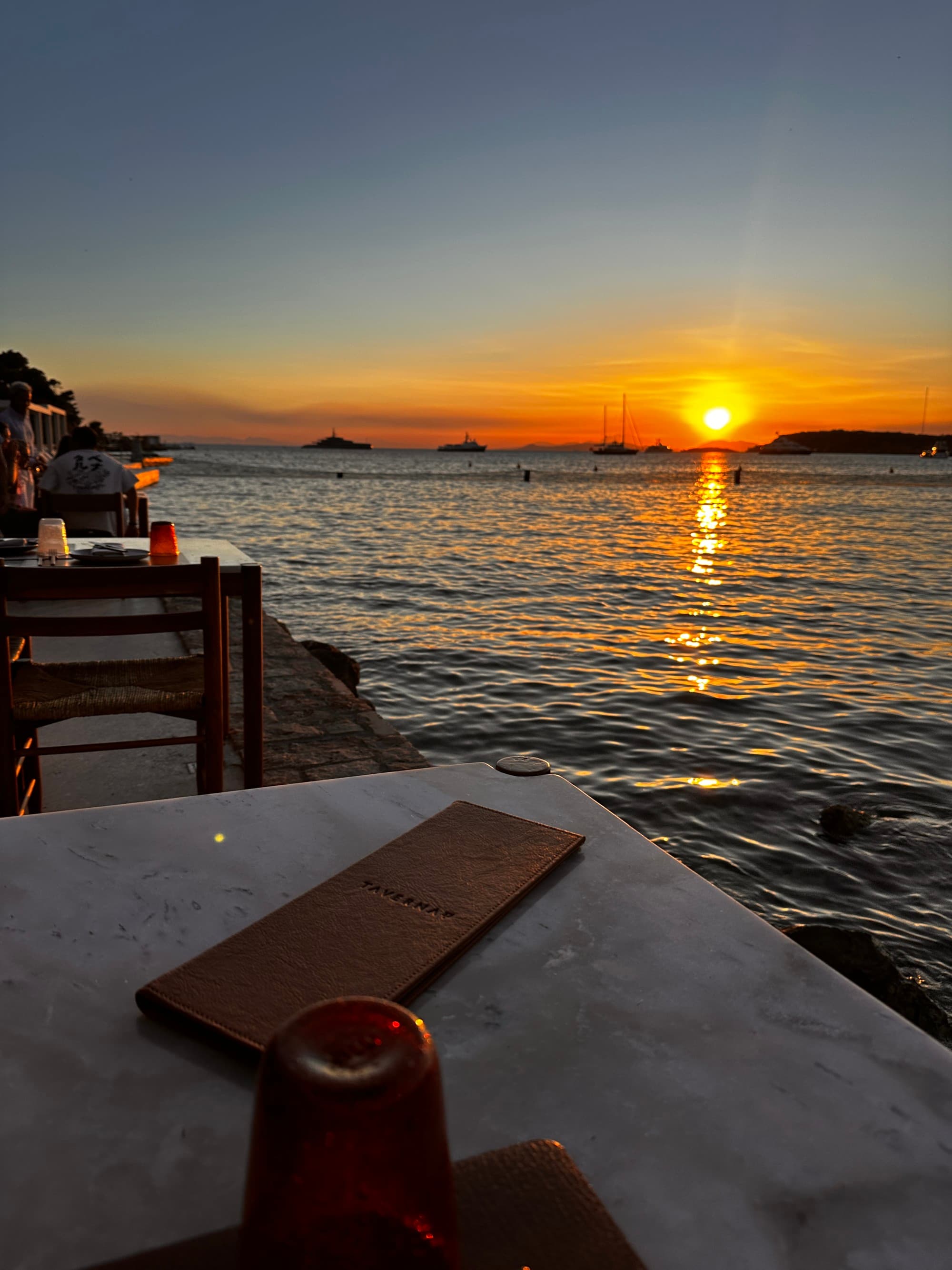 Sunset view from the seaside while sitting at a table for al fresco dining as the sun dips below the horizon on a clear day.