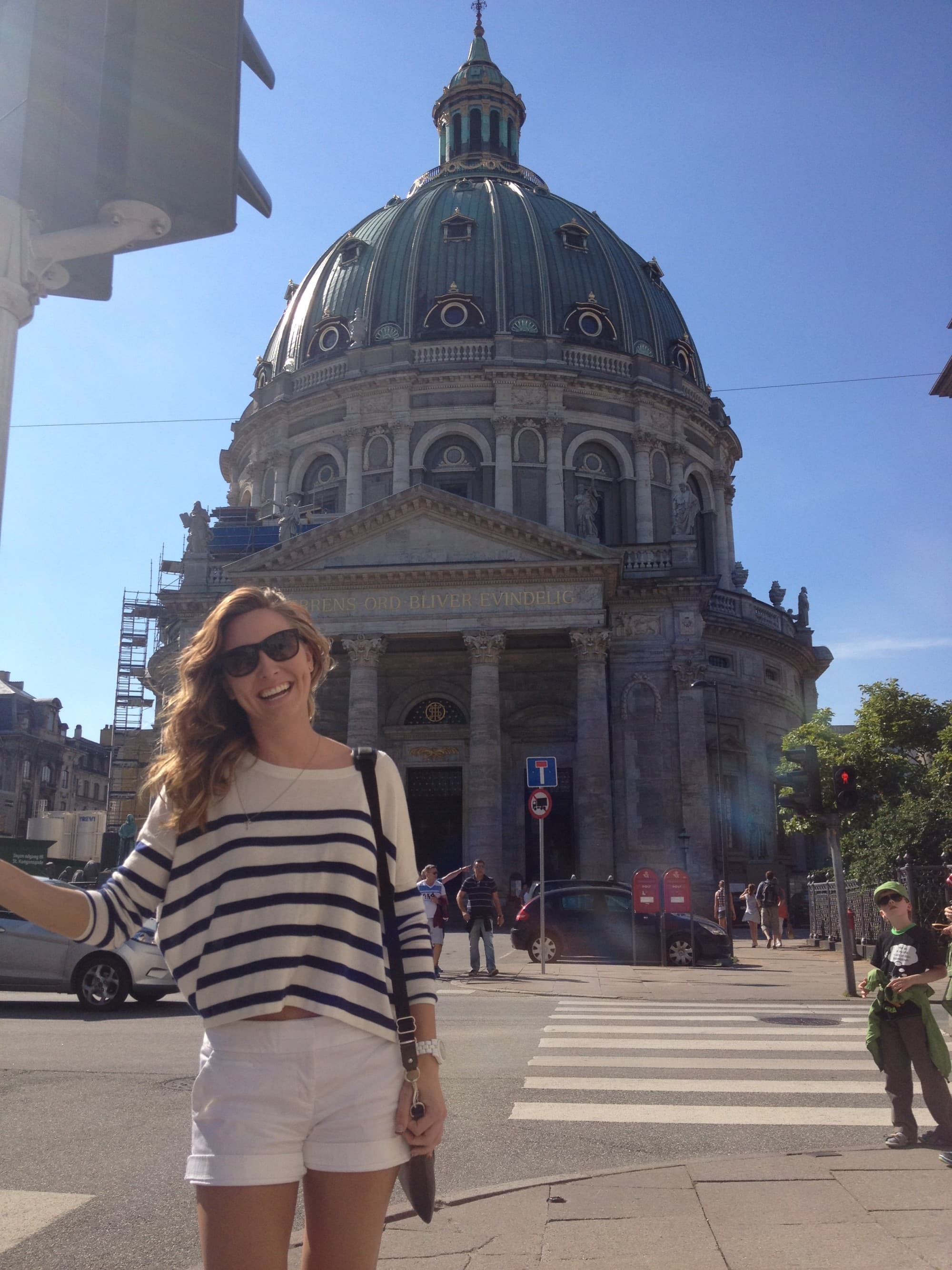 a woman in a striped shirt and white shorts stands in front of a domed building