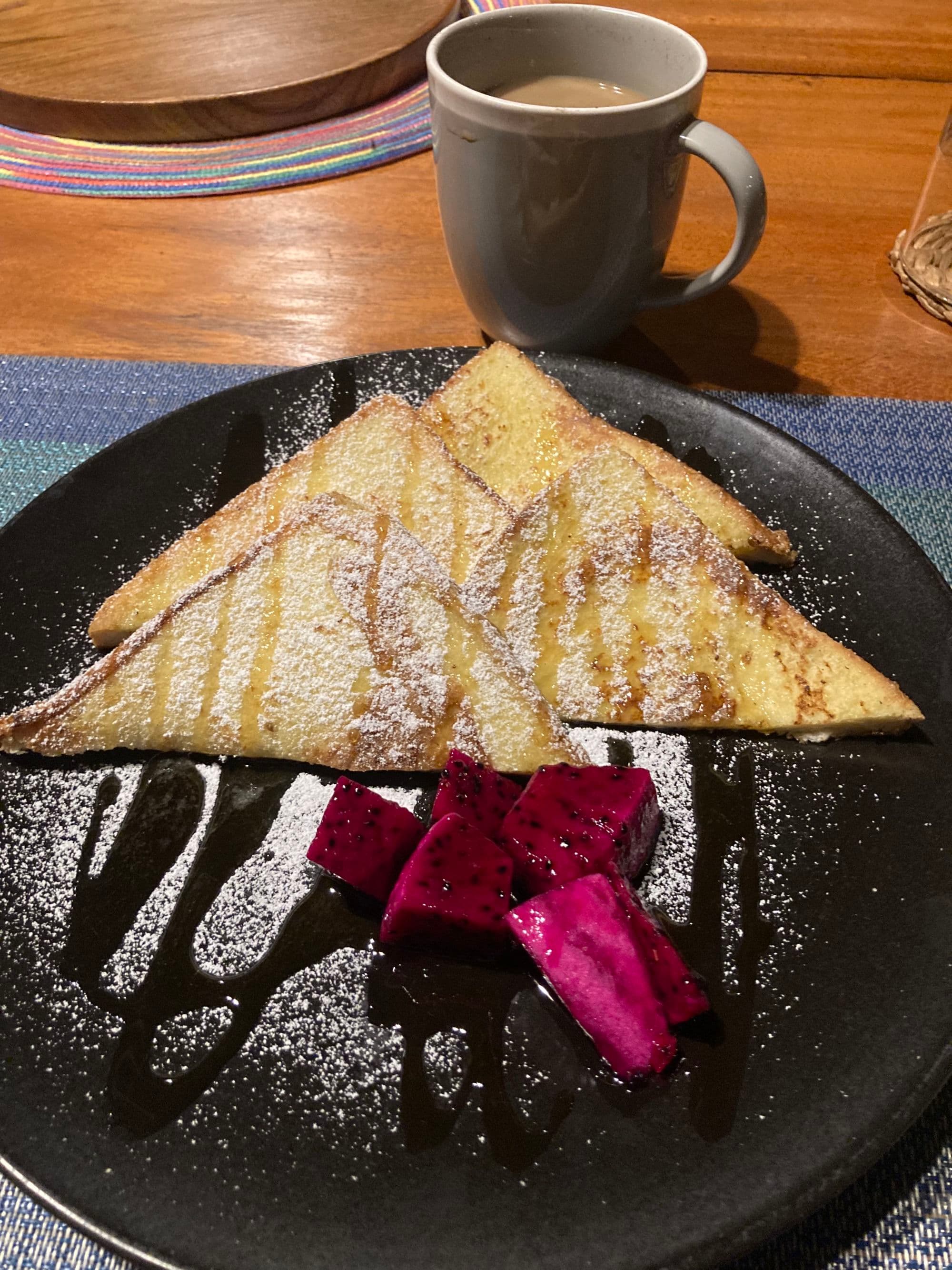 A black plate with toast and pink dragon fruit and a cup of coffee.