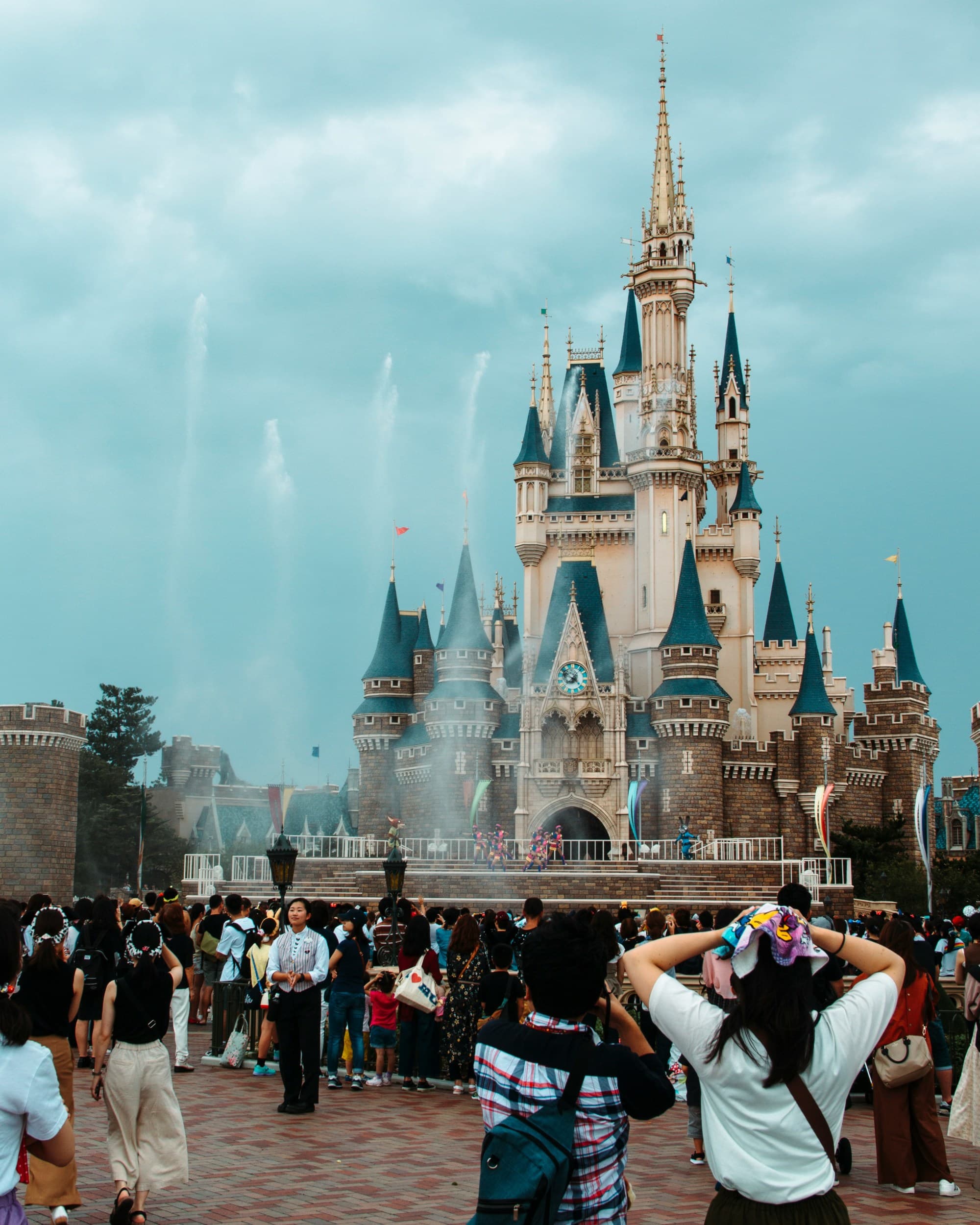 A picture of a tall castle-like building at Disney Japan with fountains and people walking around.