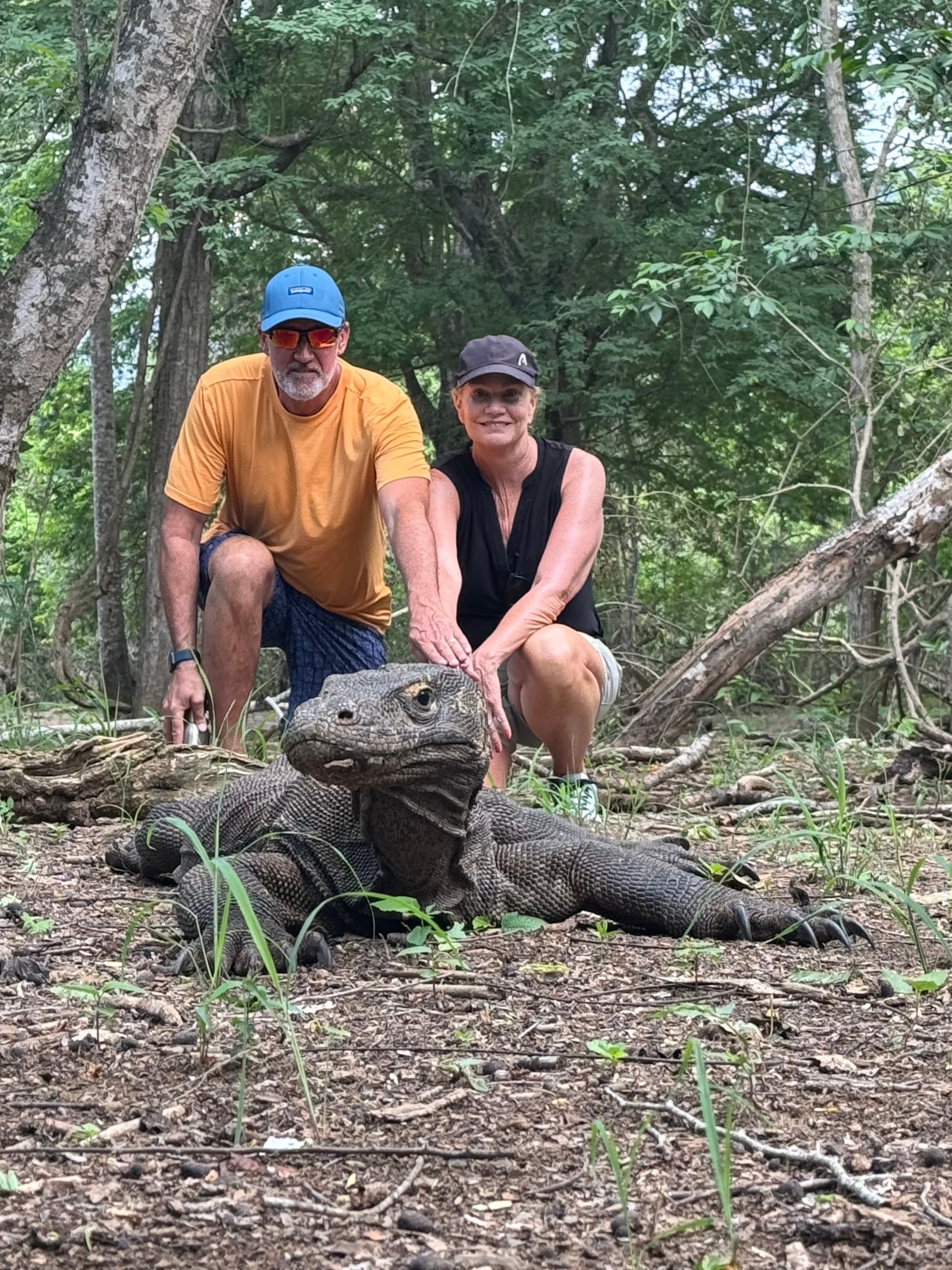 Couple poses in a forest behind a Komodo dragon.