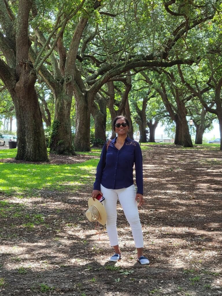 woman standing on a path with large oak trees overarching above