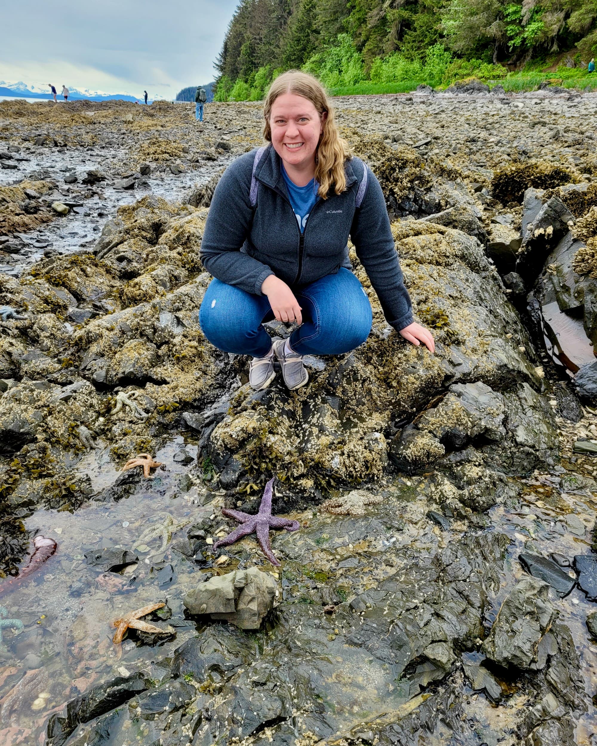 Advisor crouches on a beach next to a sea star.