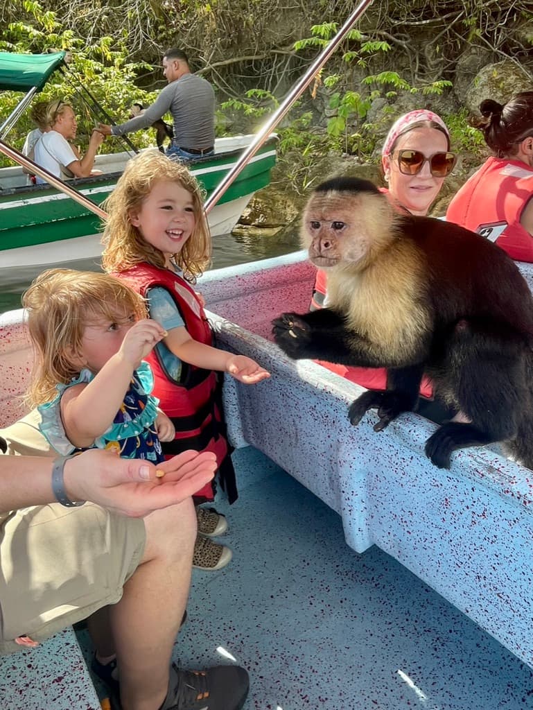 Travel advisor posing with kids on a boat adventure with a primate perched on the bench beside them.