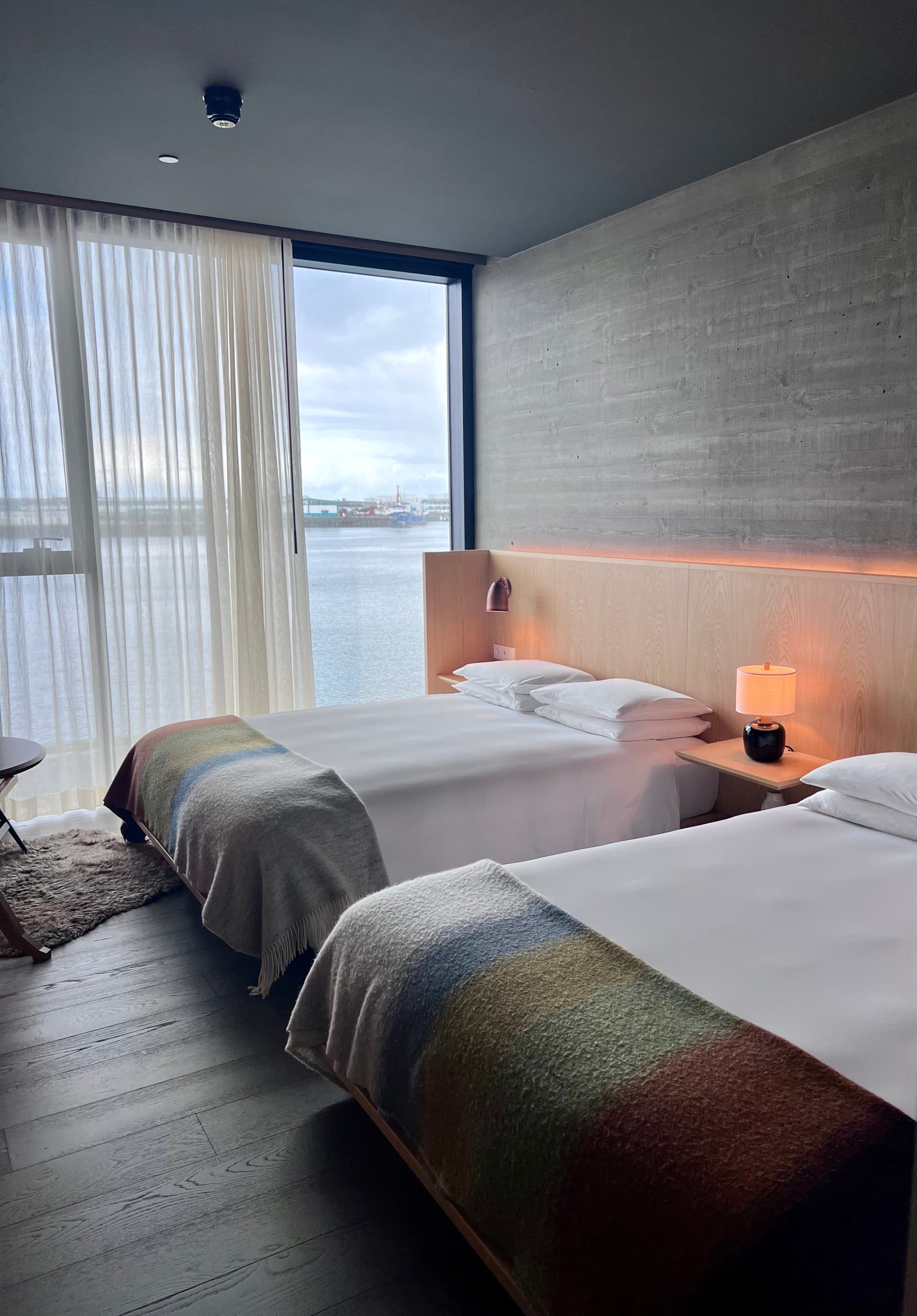 A view of a hotel room with two double beds, bedside lighting and a view of the ocean throgh the window