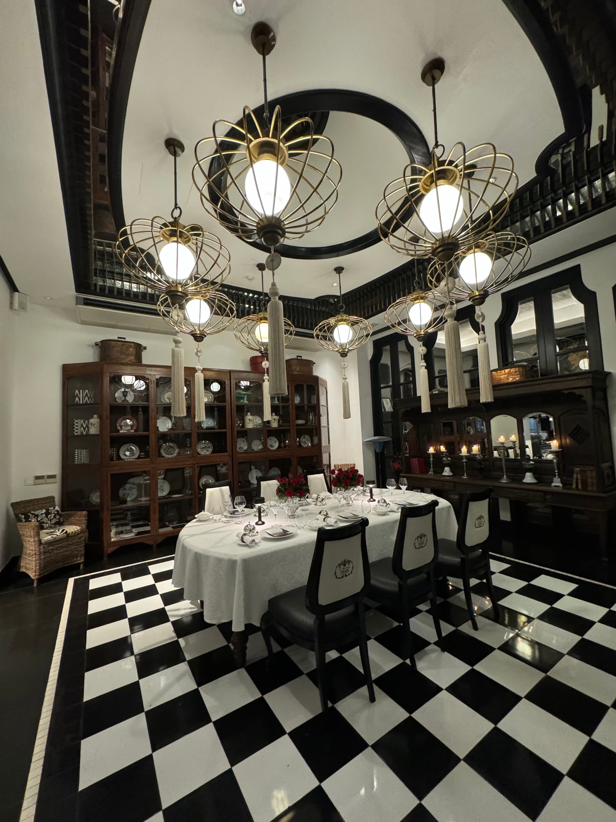An indoor dining table underneath chandeliers in a room with a wooden china cabinet and parquet floor