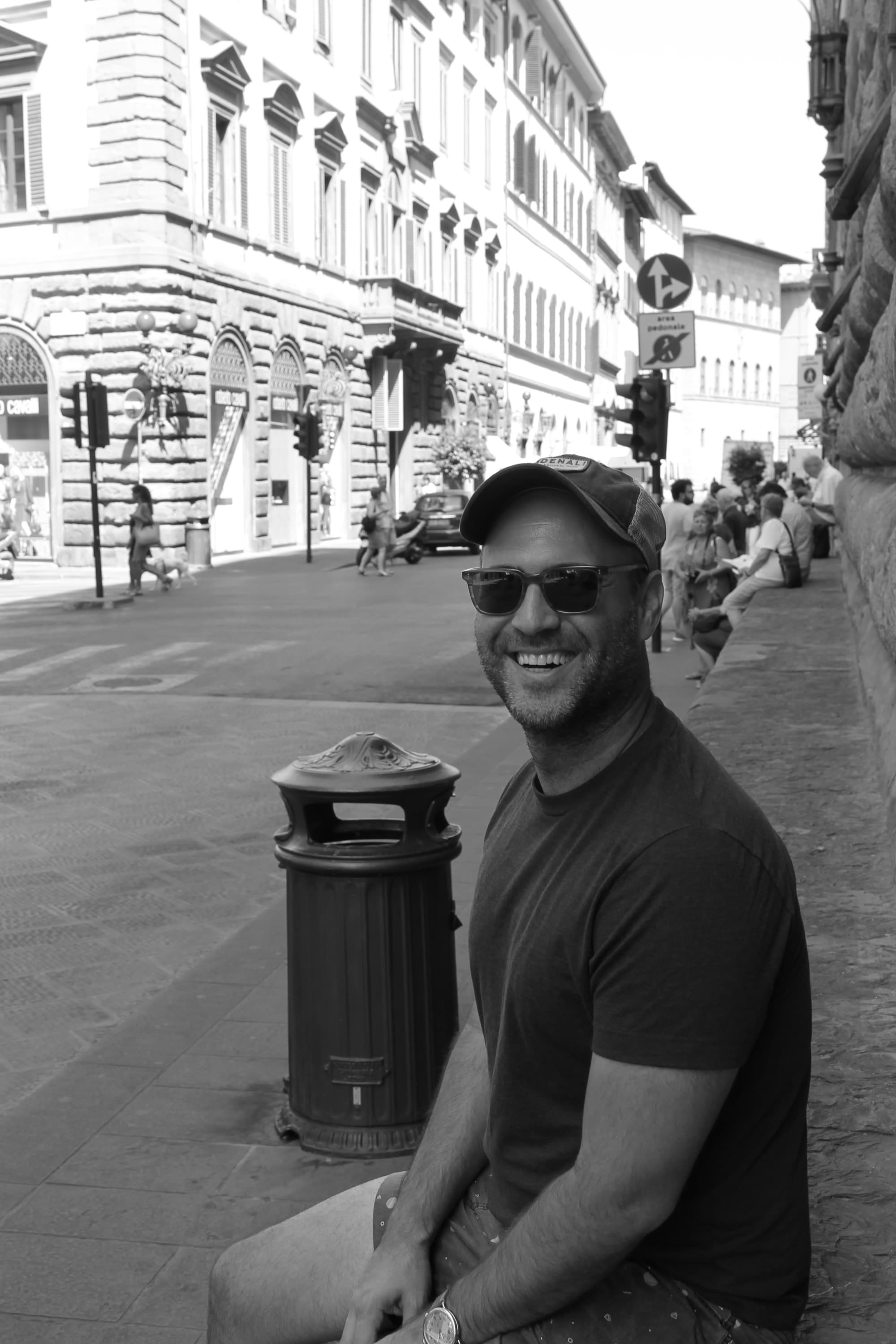 black-and-white photo of a man in sunglasses sitting on a stone bench in a city
