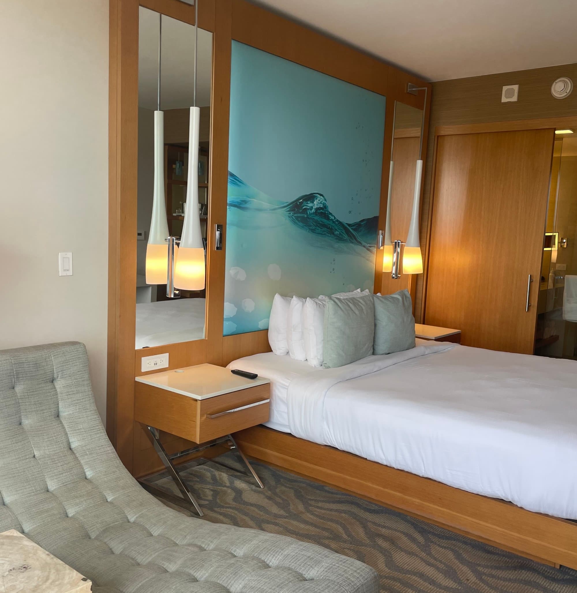 A King Room, with a white bed with wood accents and a large print of the ocean - Michelle Roe