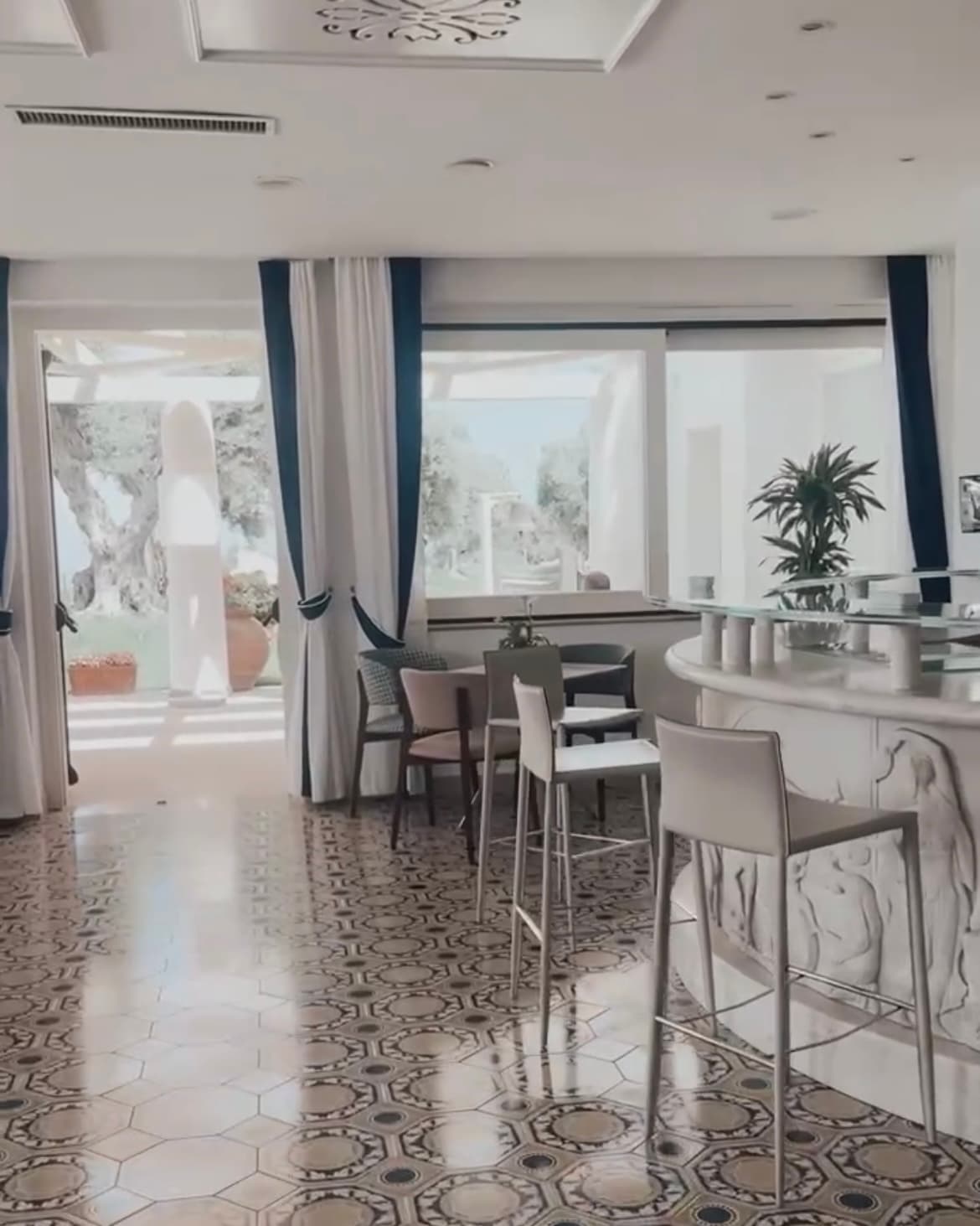 Inside the hotel's breakfast bar area with white furnishings and curtains and big, open windows looking out onto the courtyard.