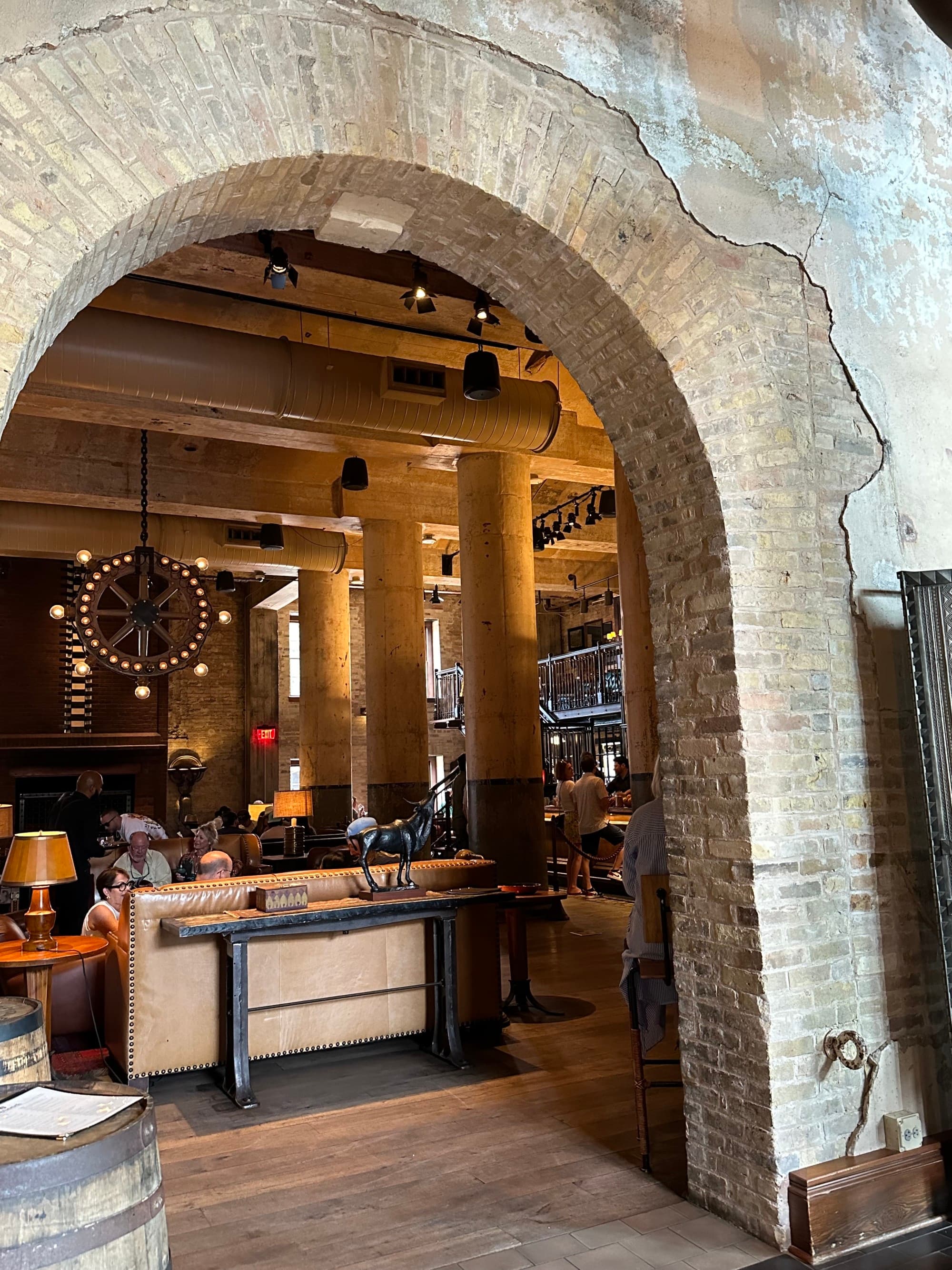 A brick archway leading into a bar area with leather sofas and dim lighting.