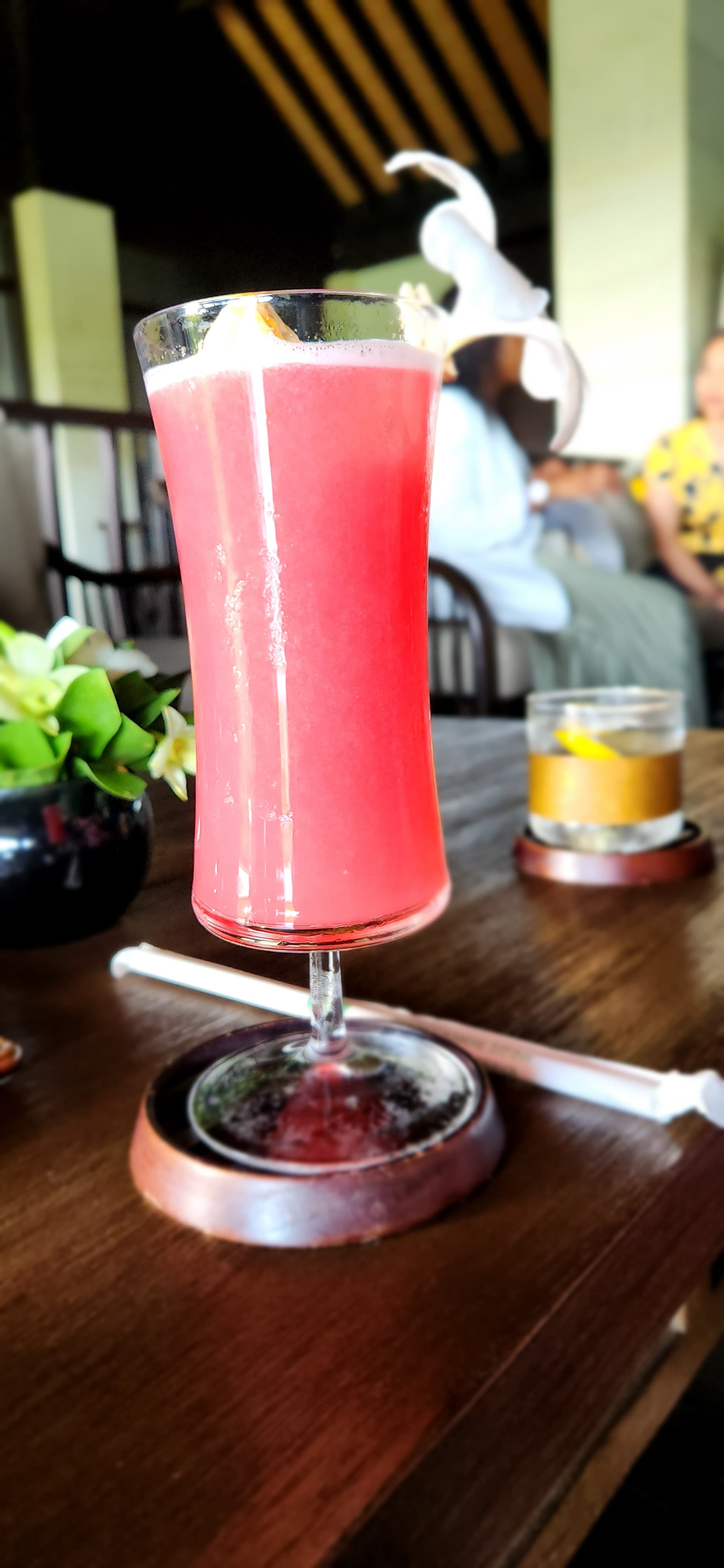 A pink drink in a tall glass sitting on a bar