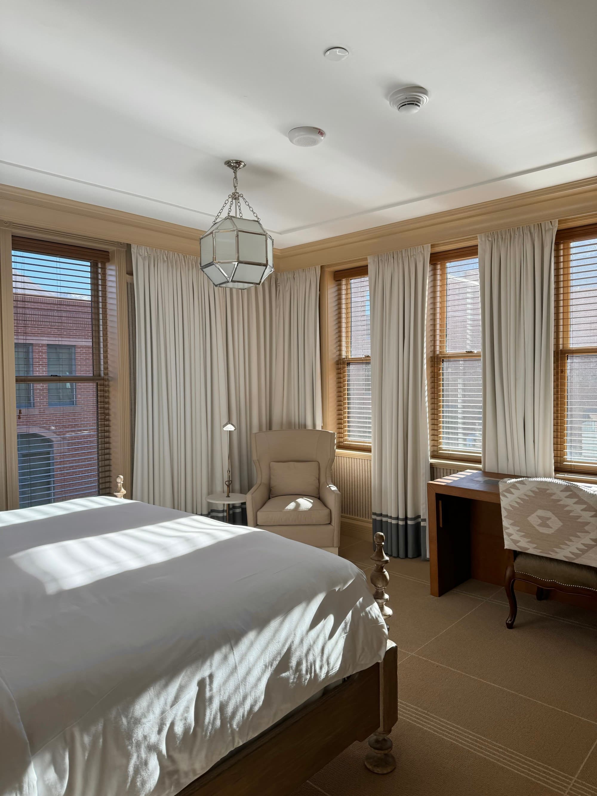 A view of the foot of the bed, with windows revealing brick buildings outside and sitting areas.