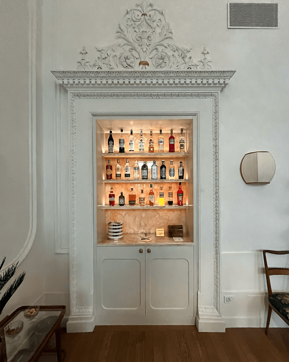 A white room with a small bar with shelves holding liquor bottles