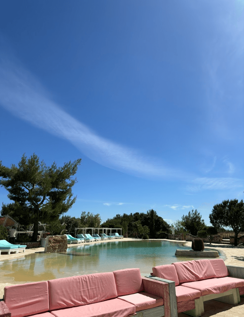 A pool designed to look like a lake with cushioned benches and lounge chairs around it on a sunny day.