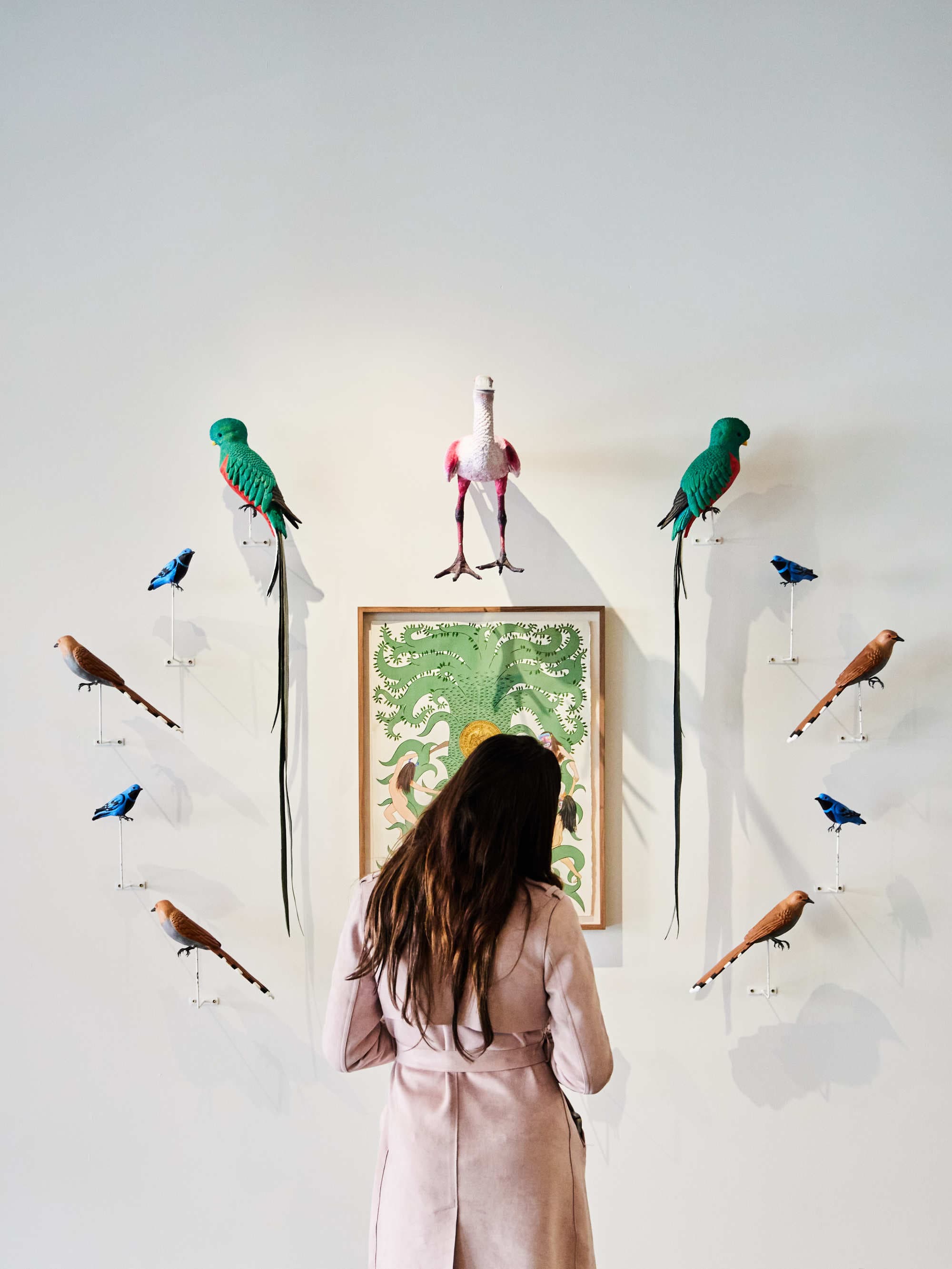 A woman standing in front of a piece of art on a wall depicting various colorful birds