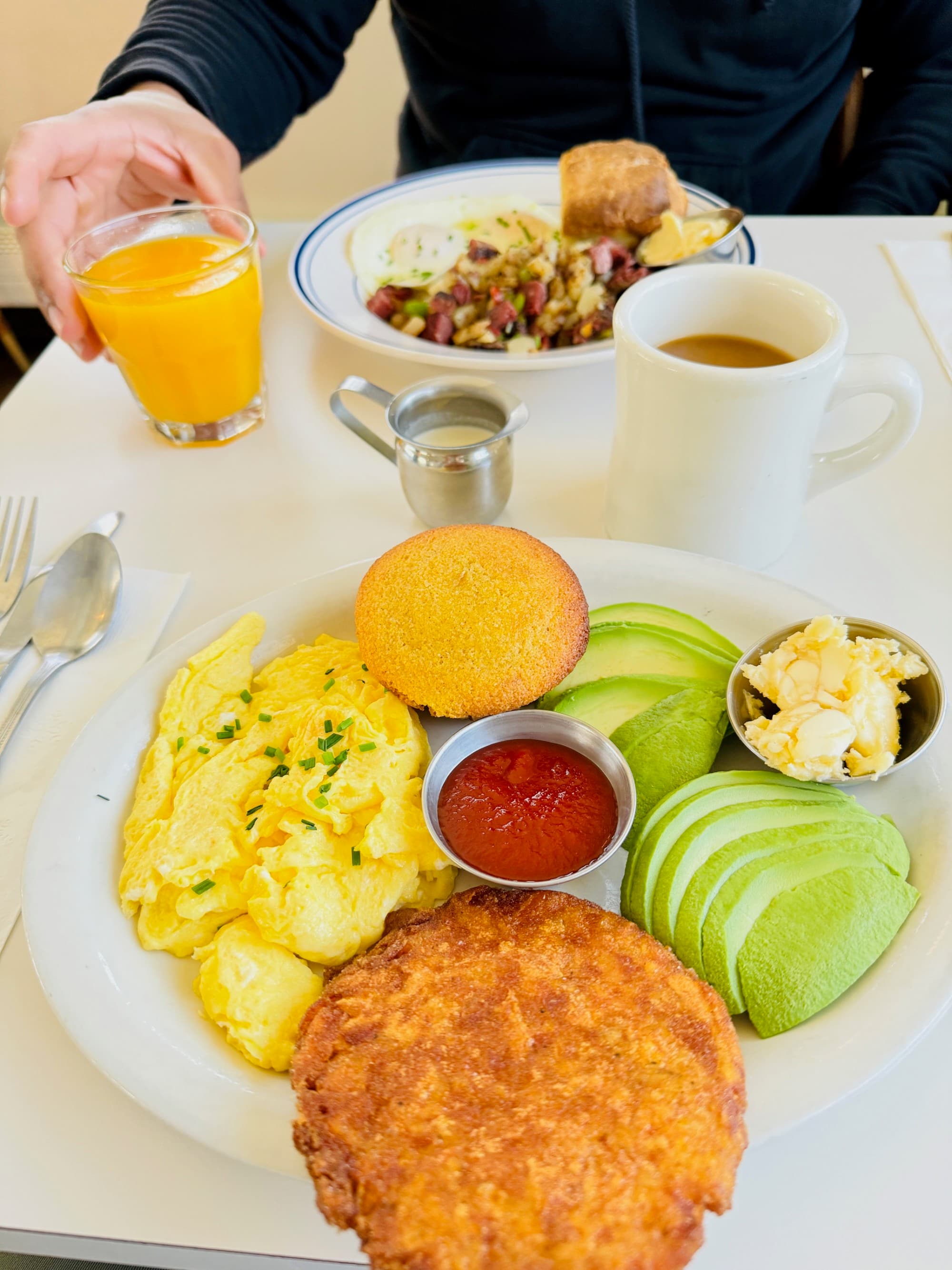 Breakfast at Gracies Luncheonette, with plates of eggs, hash browns, avocados, potatoes, juice and coffee.