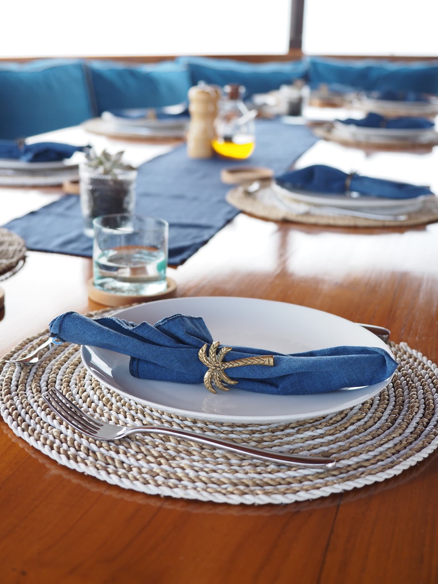 A dining room table set with white plates and blue napkins of cutlery