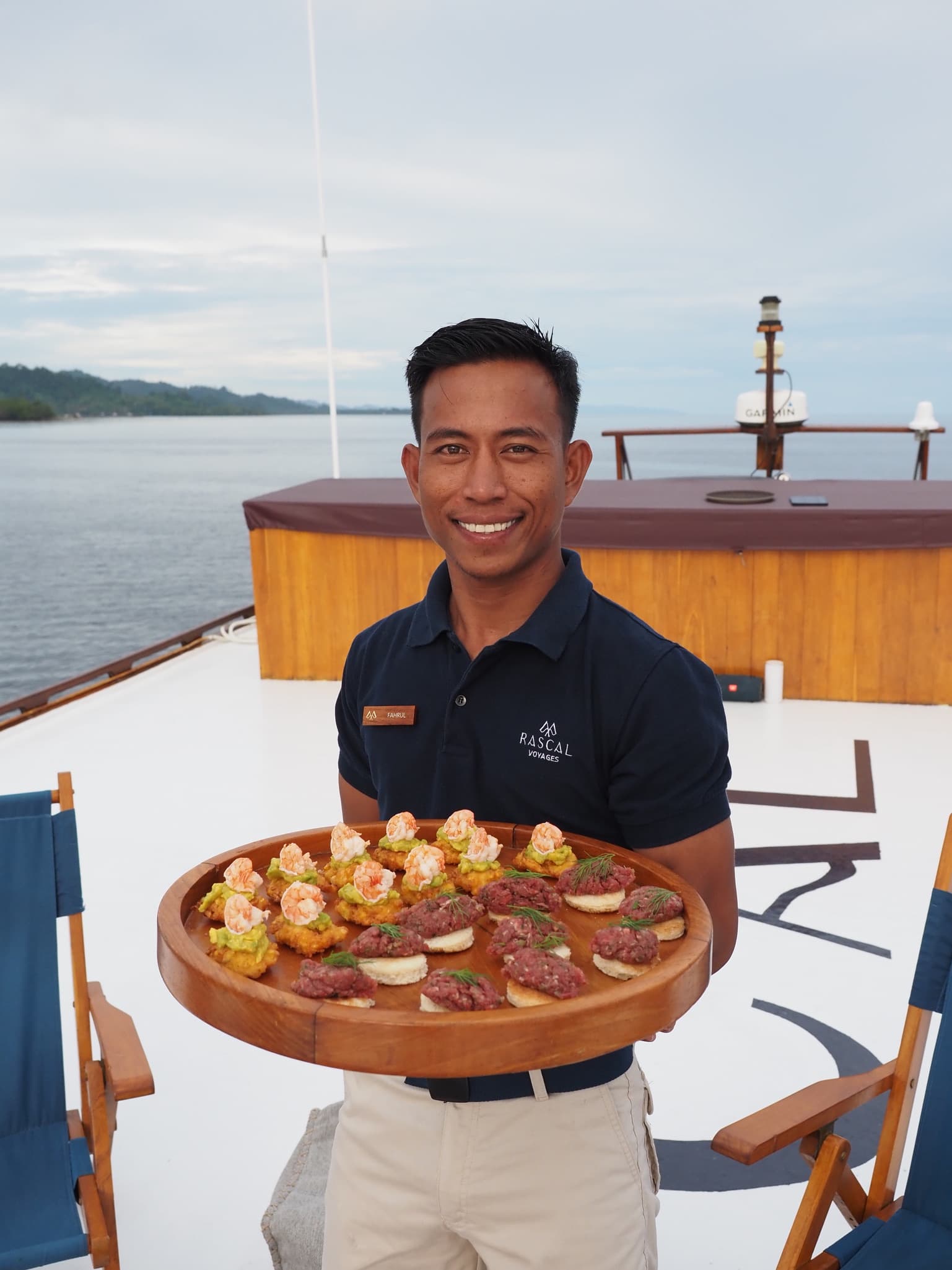 A server holding a tray of small snacks on a boat deck