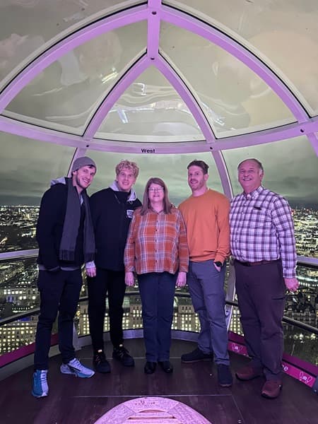 Travel advisor and family standing inside of a capsule of the London Eye, with a view of London lit up at night in the background.