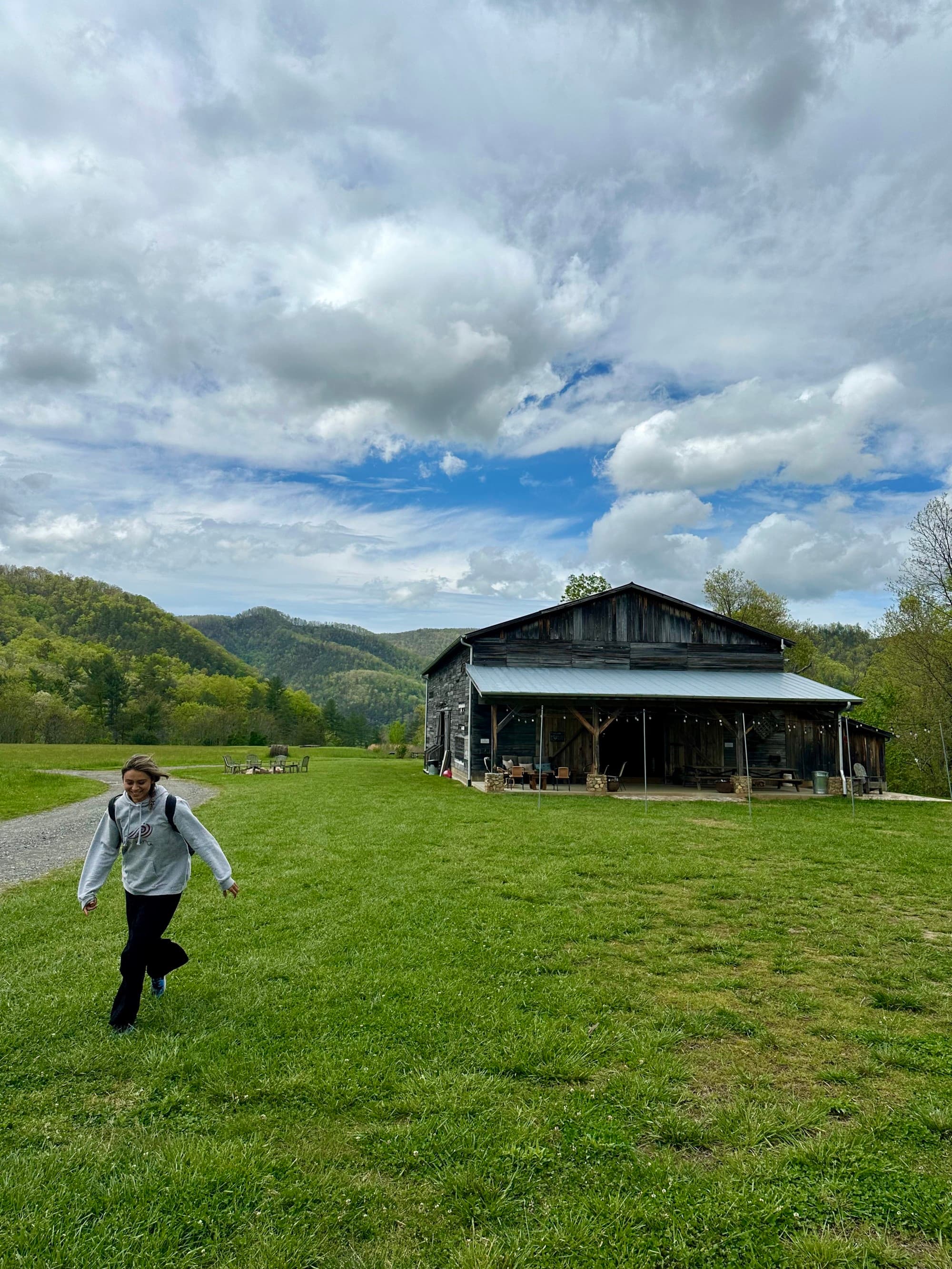 Travel Advisor's travel buddy walking through an open, green, grassy field with a wooden cabin in the background, underneath a mostly-cloudy sky.
