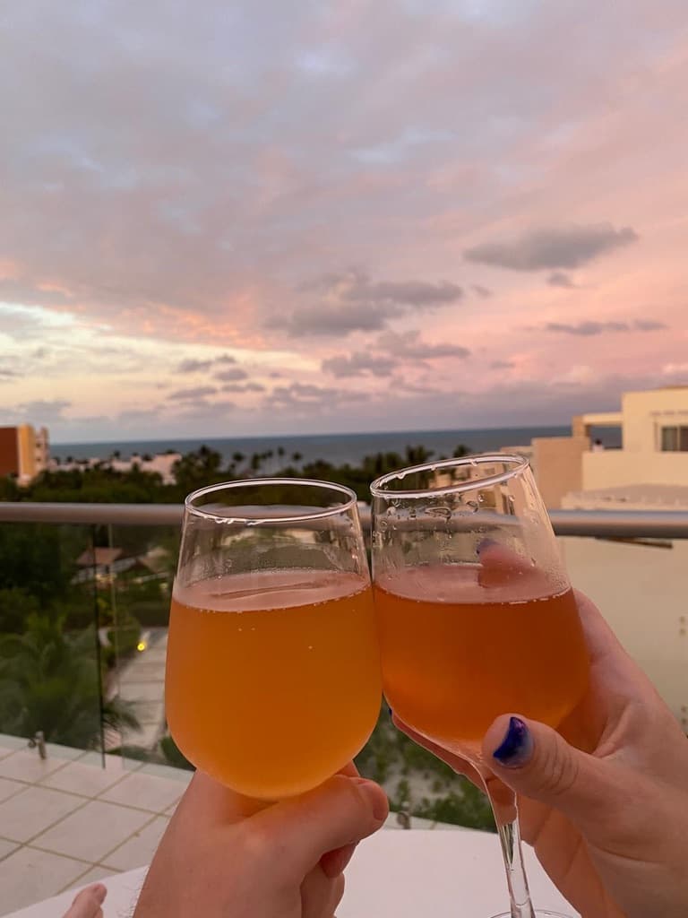 Two glasses full of an orange and red drink, clinking in front of a sunset sky