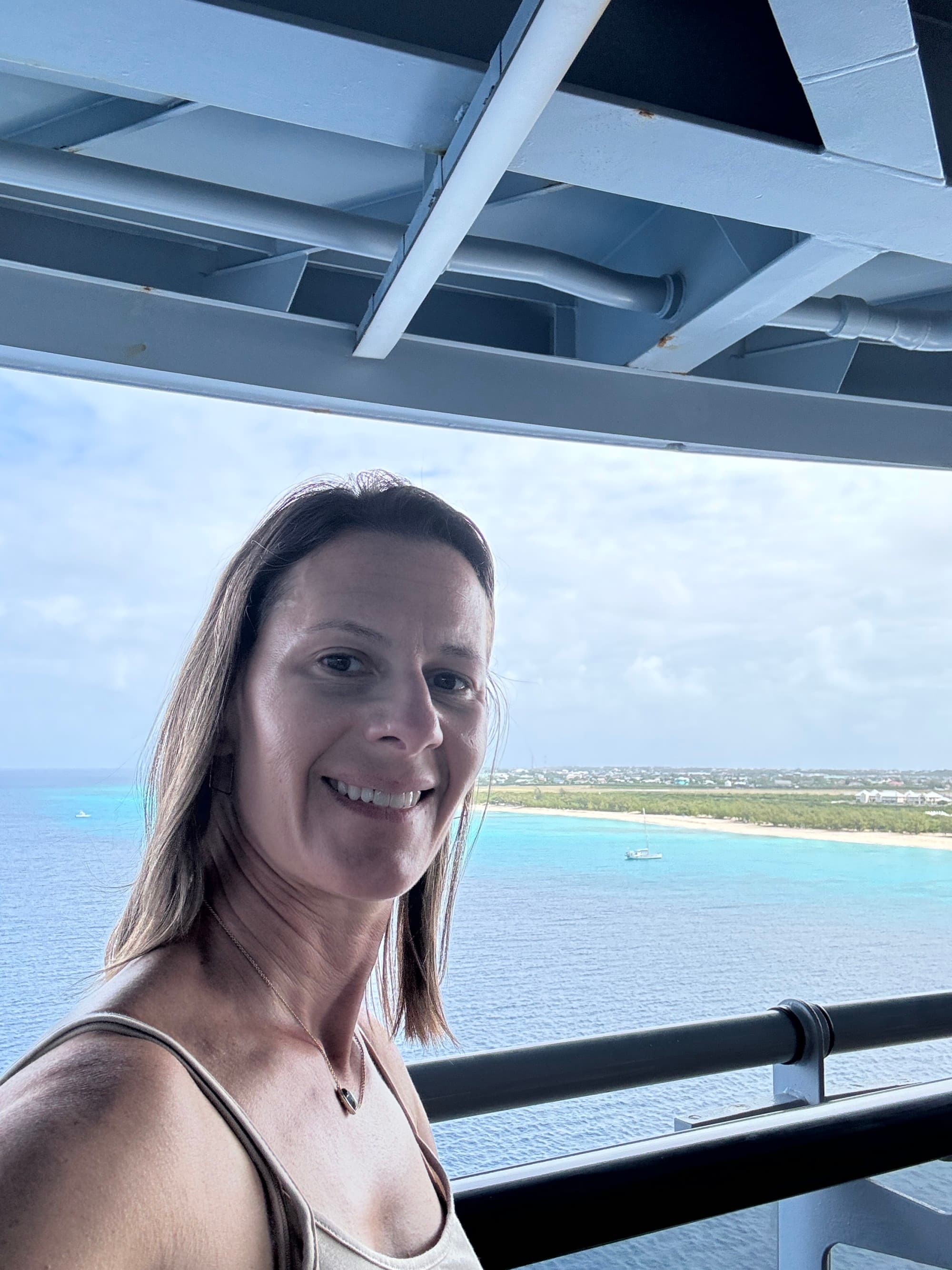 Travel advisor aboard Virgin Voyages, on the deck with the sea and coastline in the background.