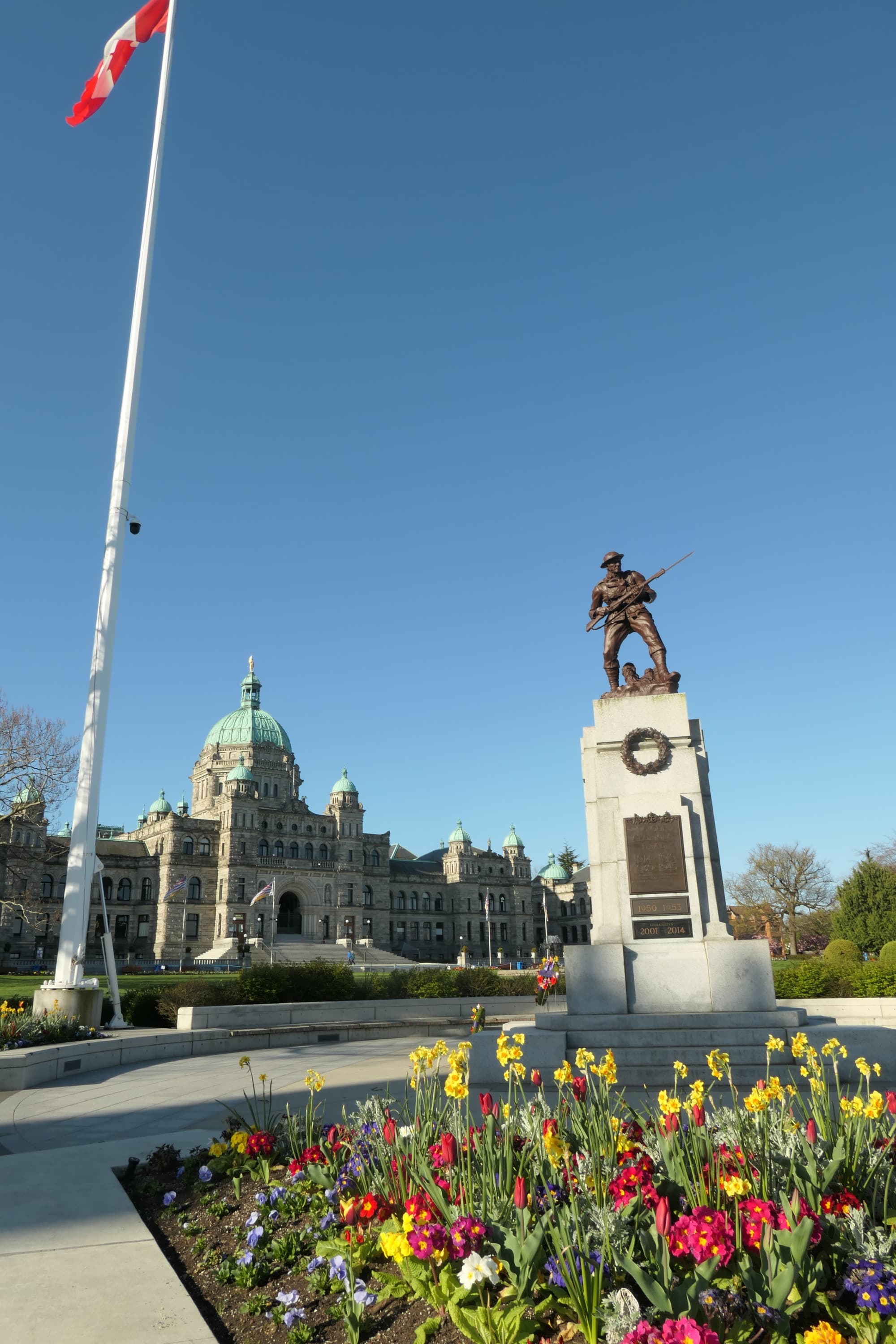 A statue of a man holding a rifle in a town square in front of an ornate building with a green roof.