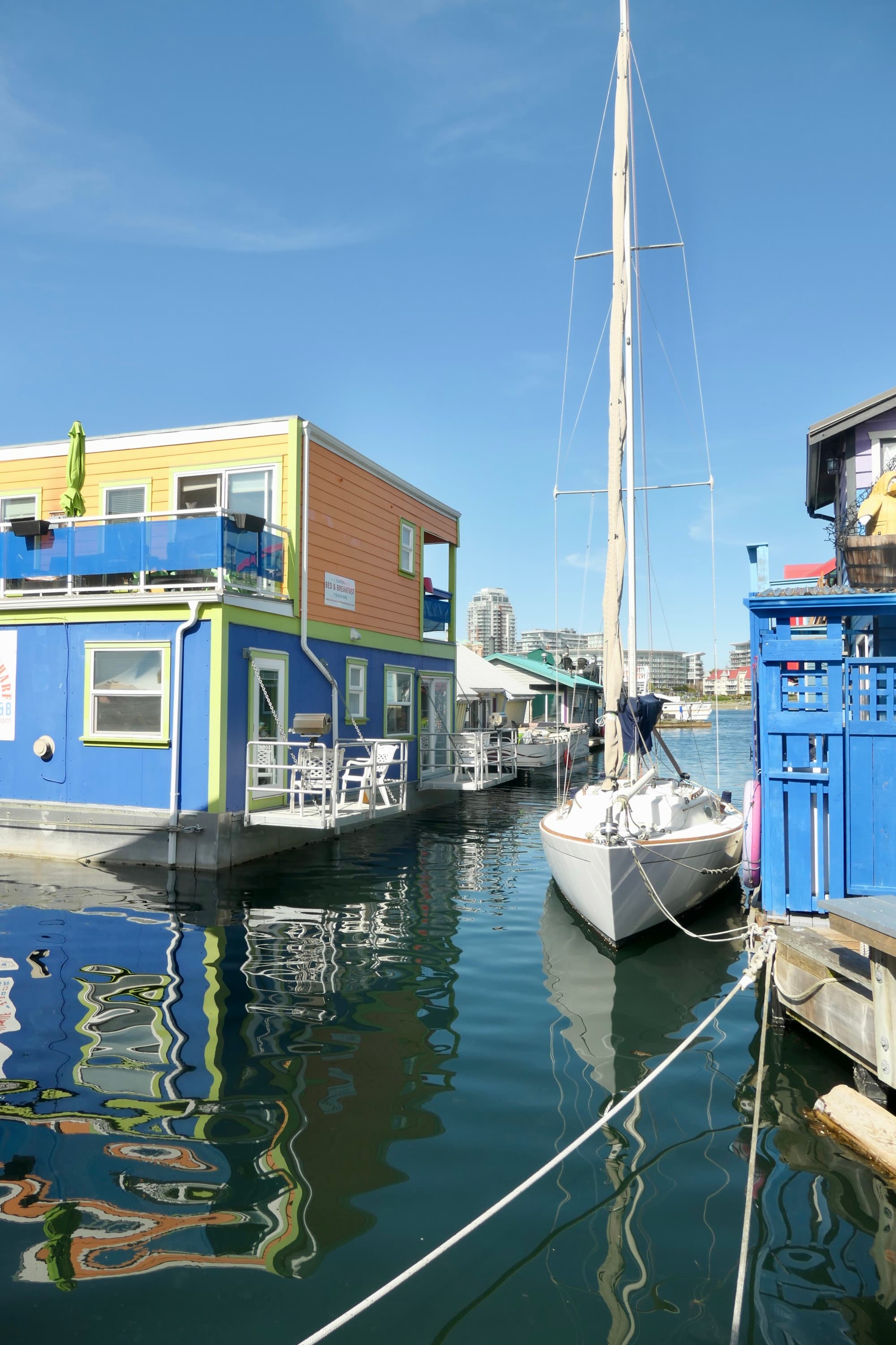 A sailboat in waiter between blue and yellow houseboats