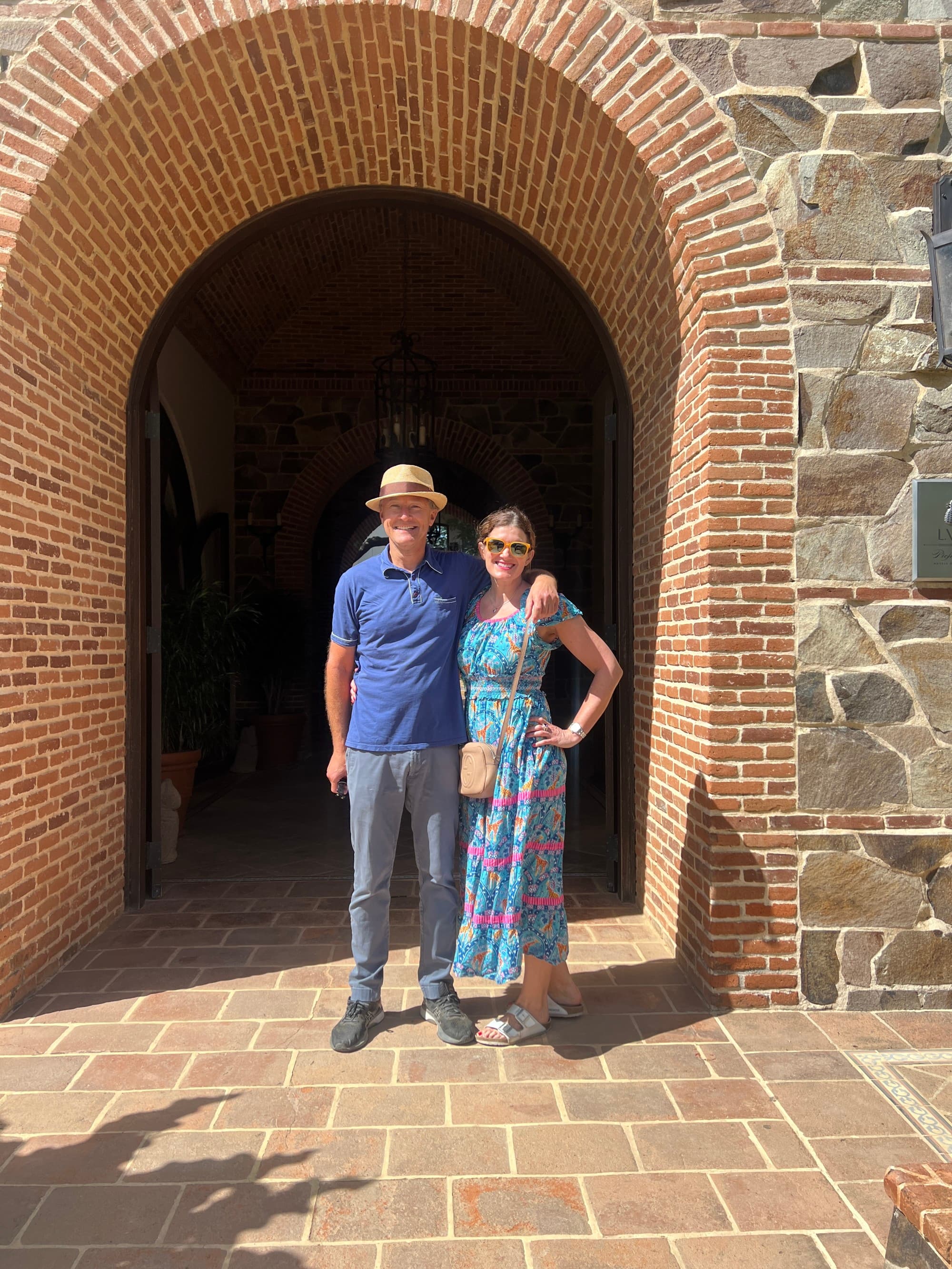A couple posing under a large brick archway of a building made of stone