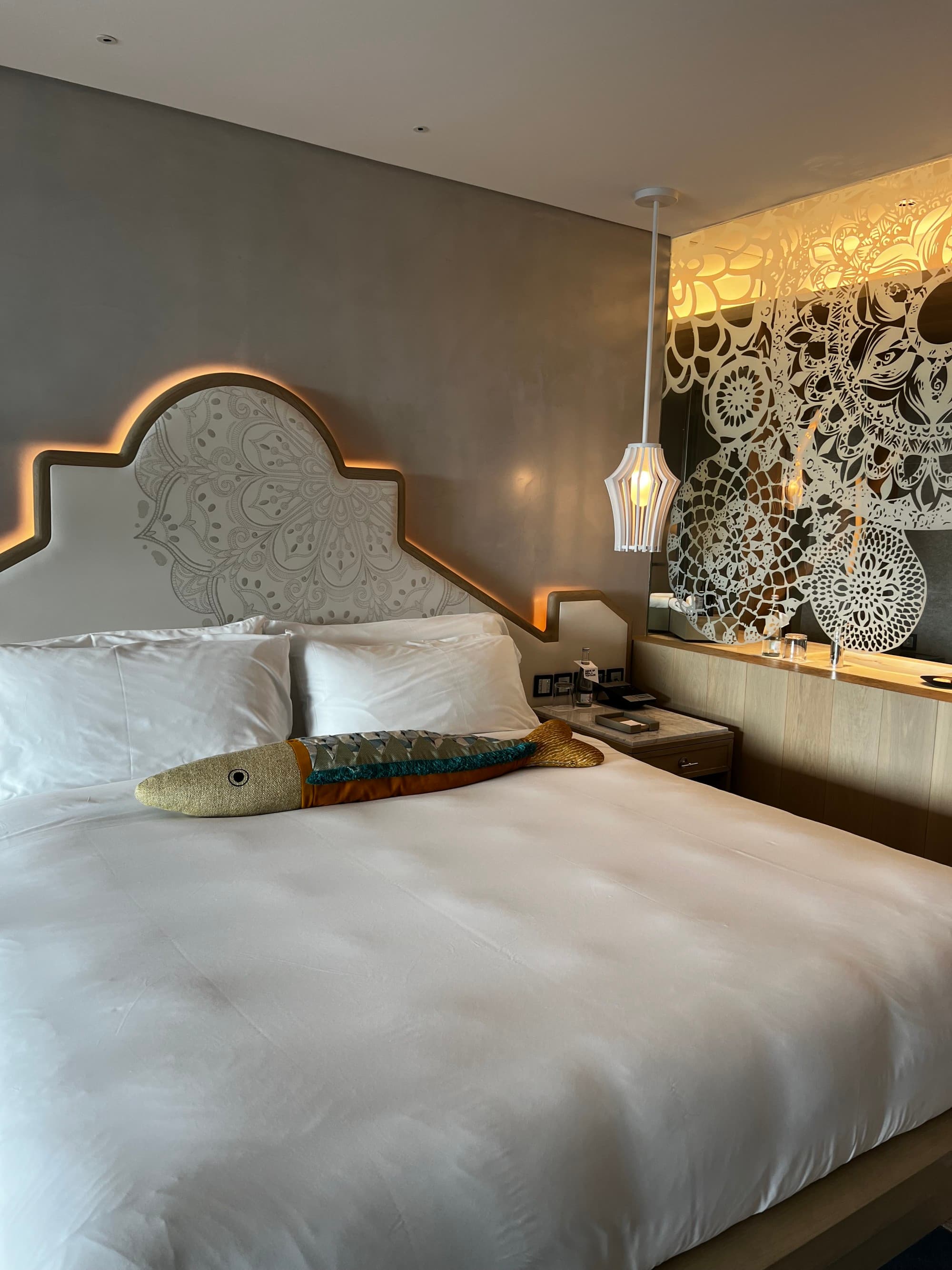 A room with a gray bed, fish-shaped accent pillow and Portuguese-inspired abstract art on the wall