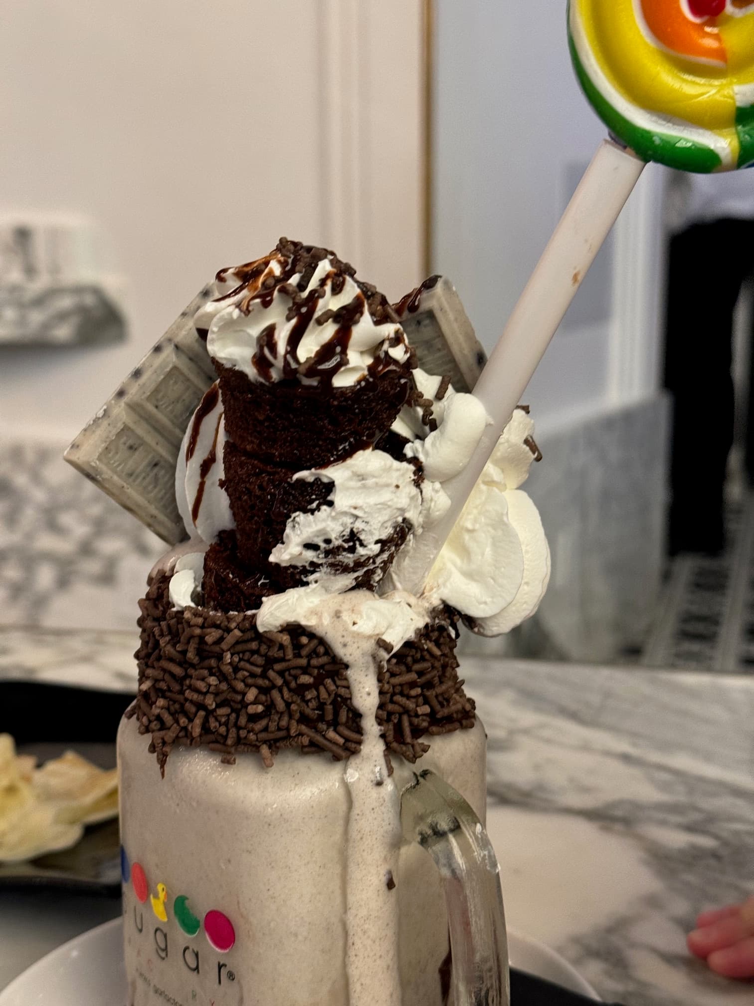 A cookies and cream milkshake with various chocolate sprinkles, whipped cream, oreo cookies, chocolate bars and a straw coming out of it.
