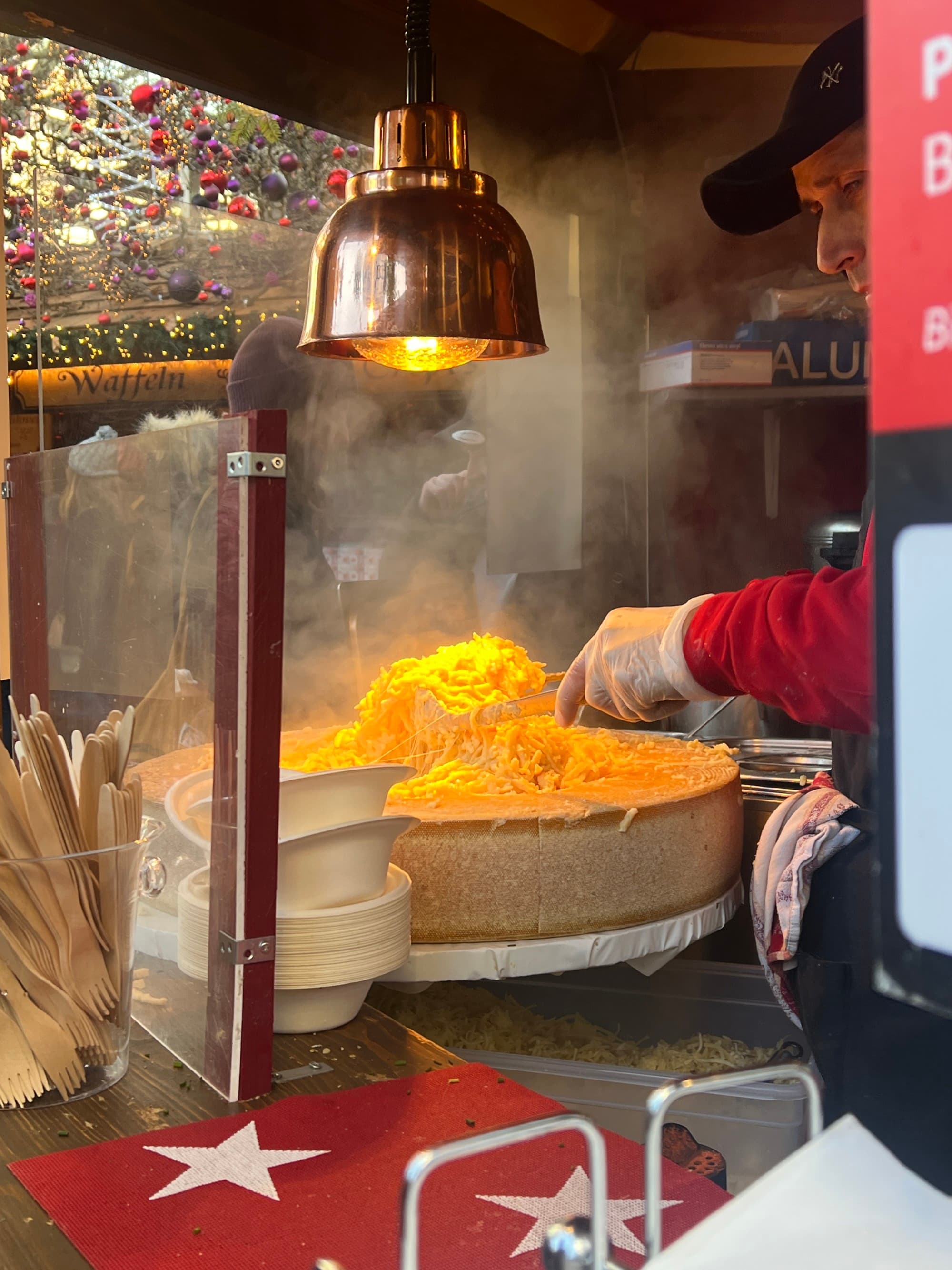 An image of pasta inside of a cheese wheel beneath a heat lamp. Someone is cooking the food.