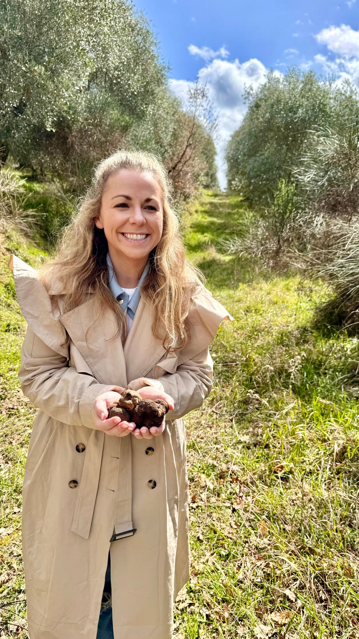 a woman in a tan coat holds black truffles in her hands