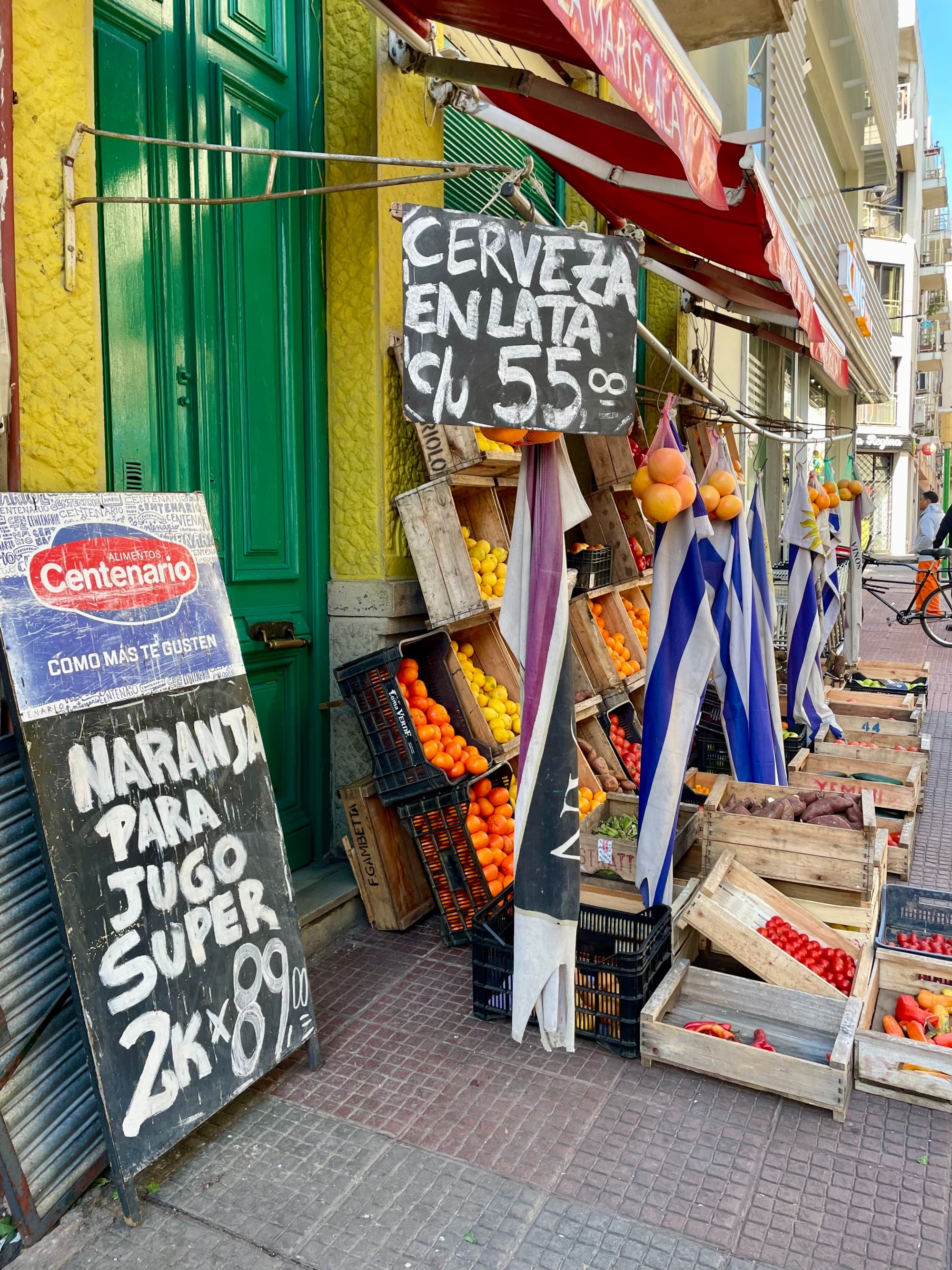 A city street with black and white signs, crates of produce and a green door.